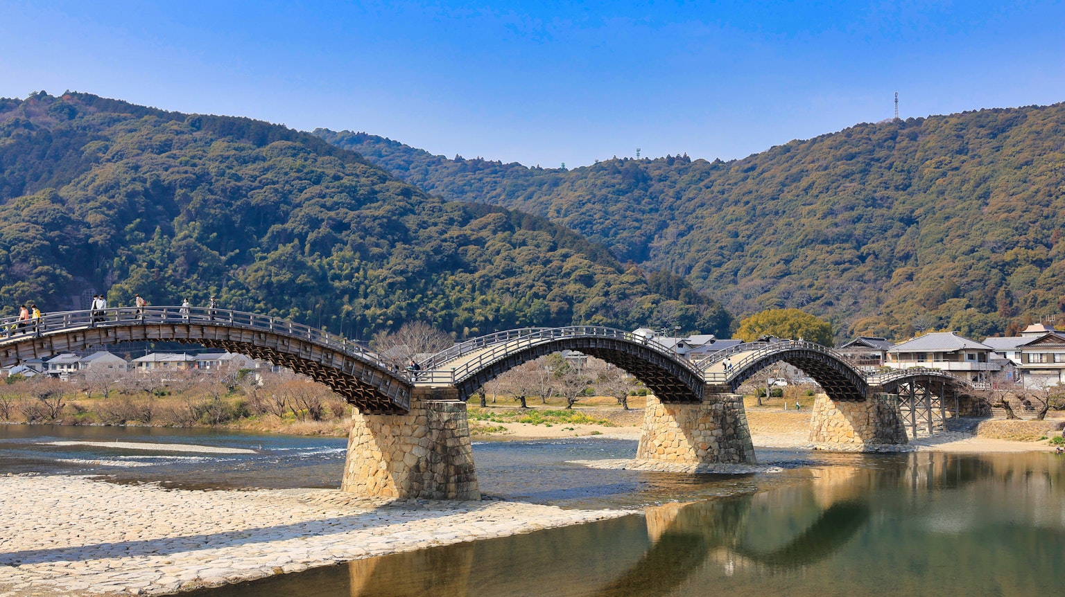 Un hermoso puente en arco cruza un río con montañas y un cielo azul de fondo
