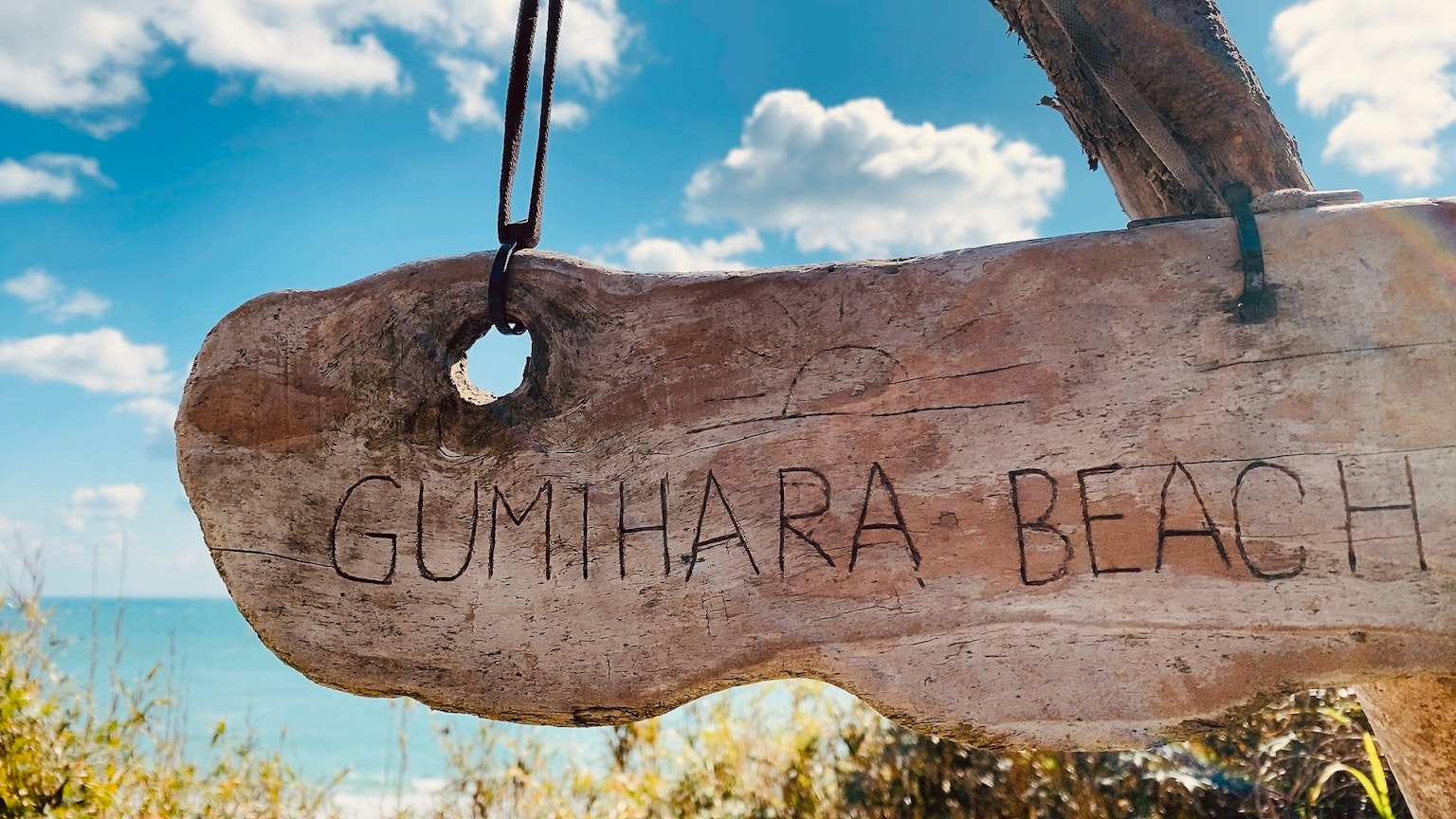 Insegna in legno per la spiaggia di Gunthara con sfondo di cielo blu e oceano