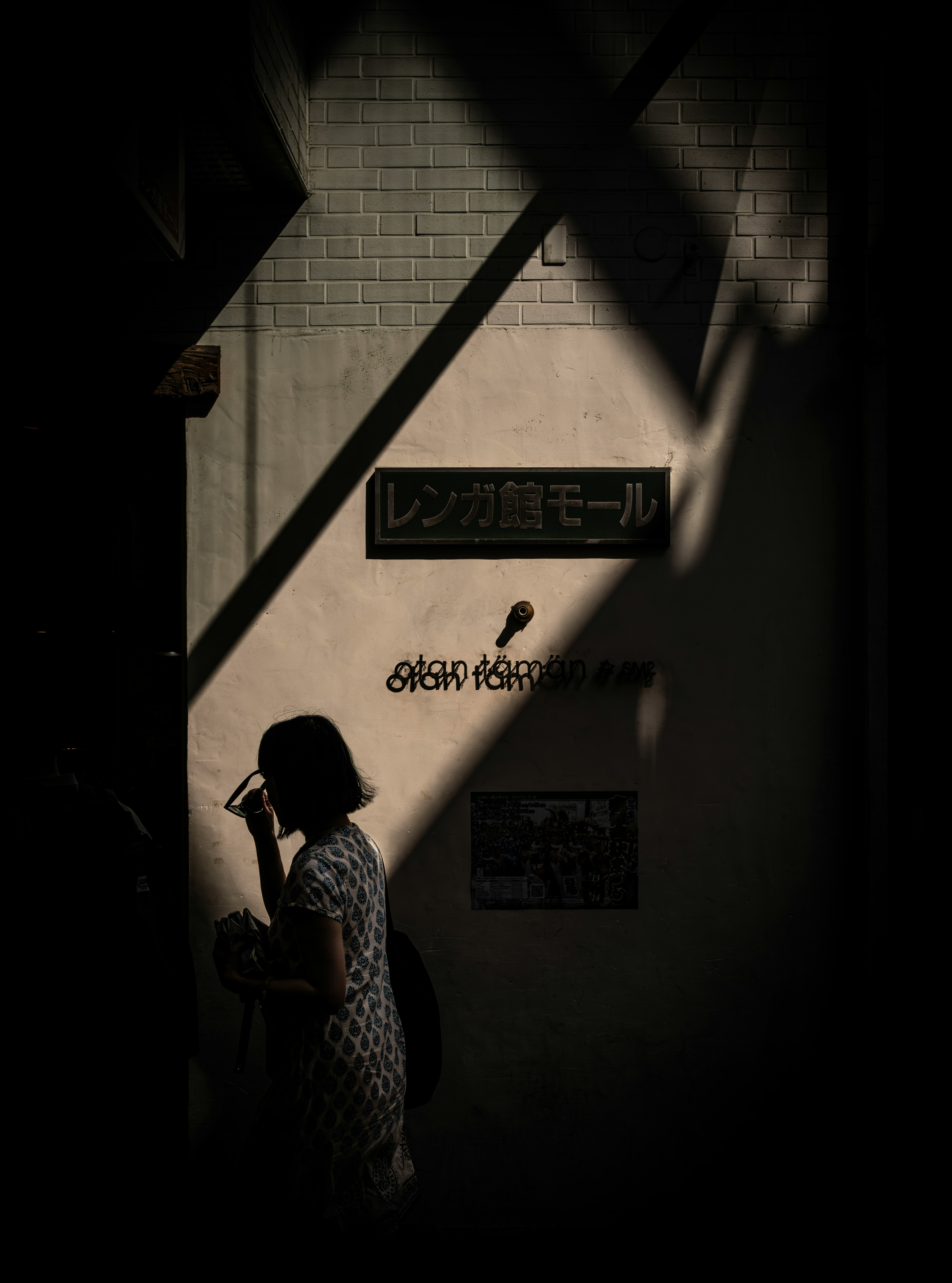 壁の影の中で立つ人物と看板のある路地