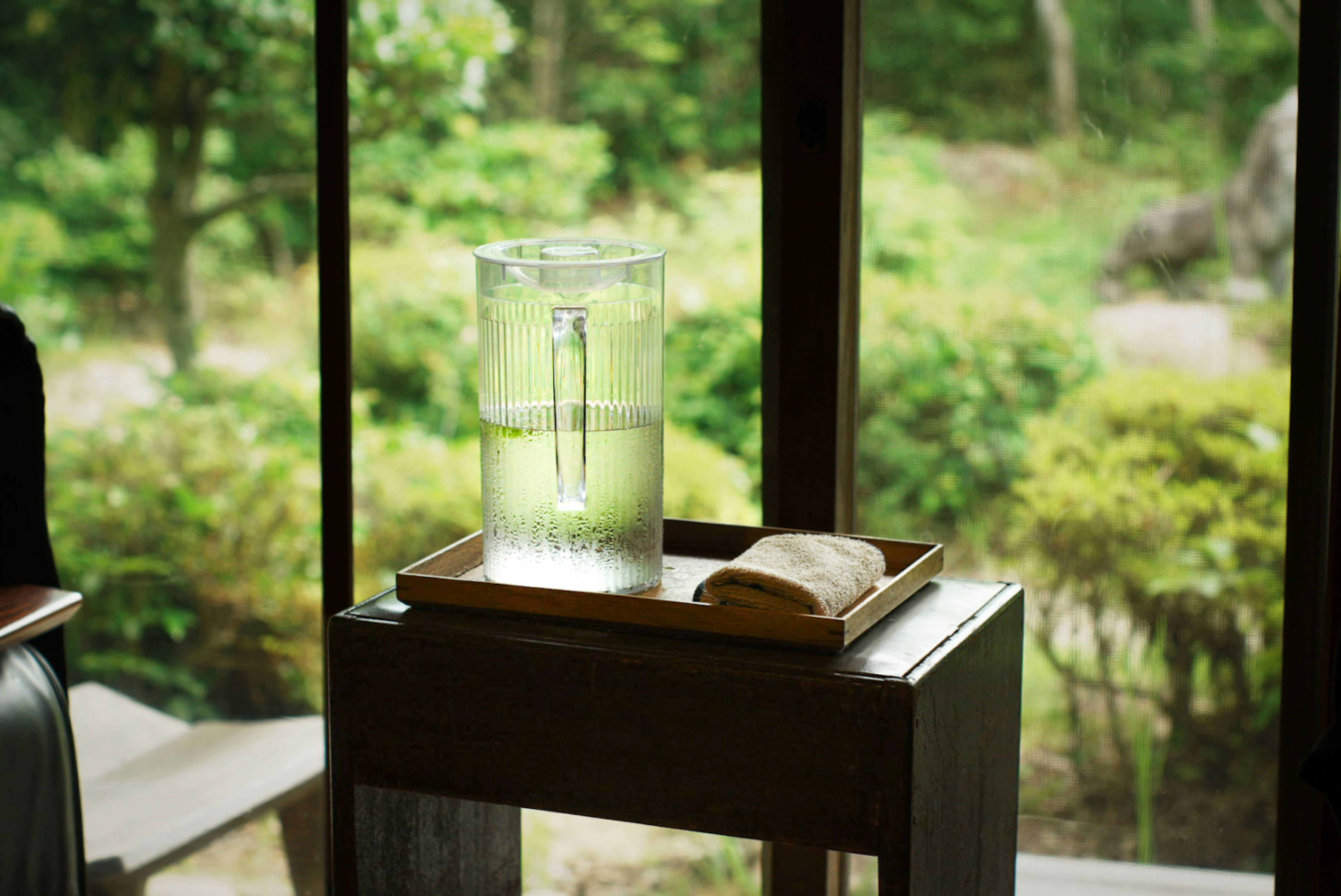 Glas mit Wasser und sichtbaren Wassertropfen auf einem Holztablett neben einem Fenster