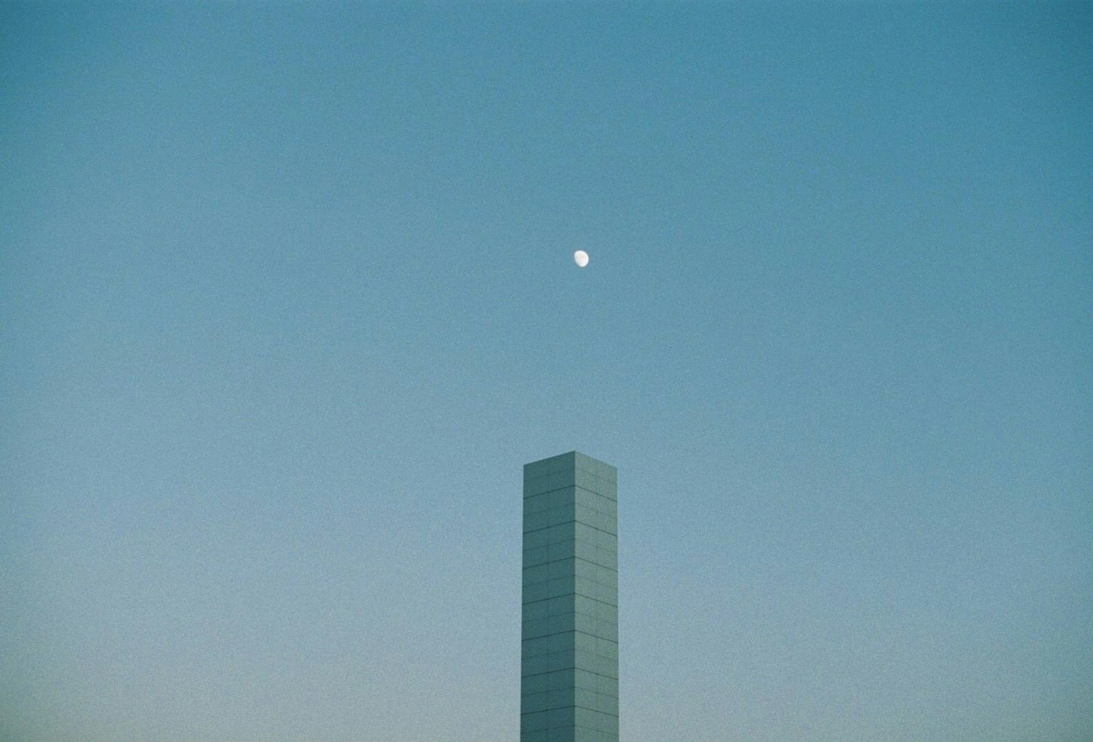 Silueta de un edificio alto contra un cielo azul con una luna visible