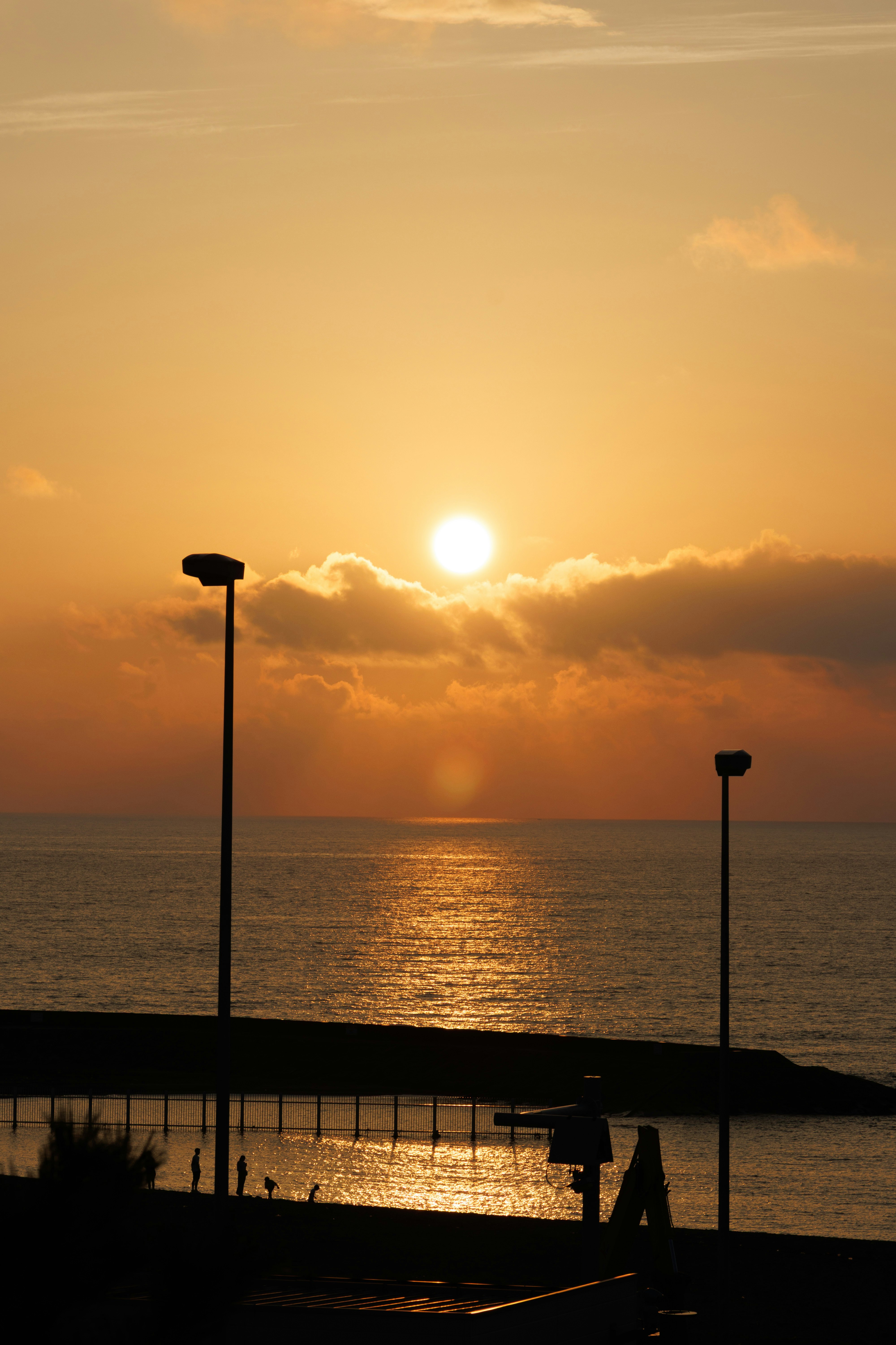 夕日に照らされる海辺の遊歩道と街灯のシルエット