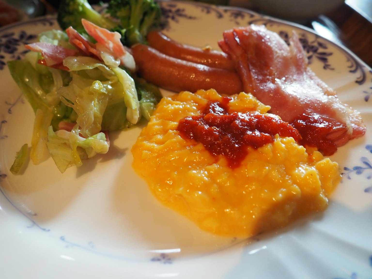 Un piatto con insalata, salsicce, bacon e purè giallo guarnito con salsa di pomodoro