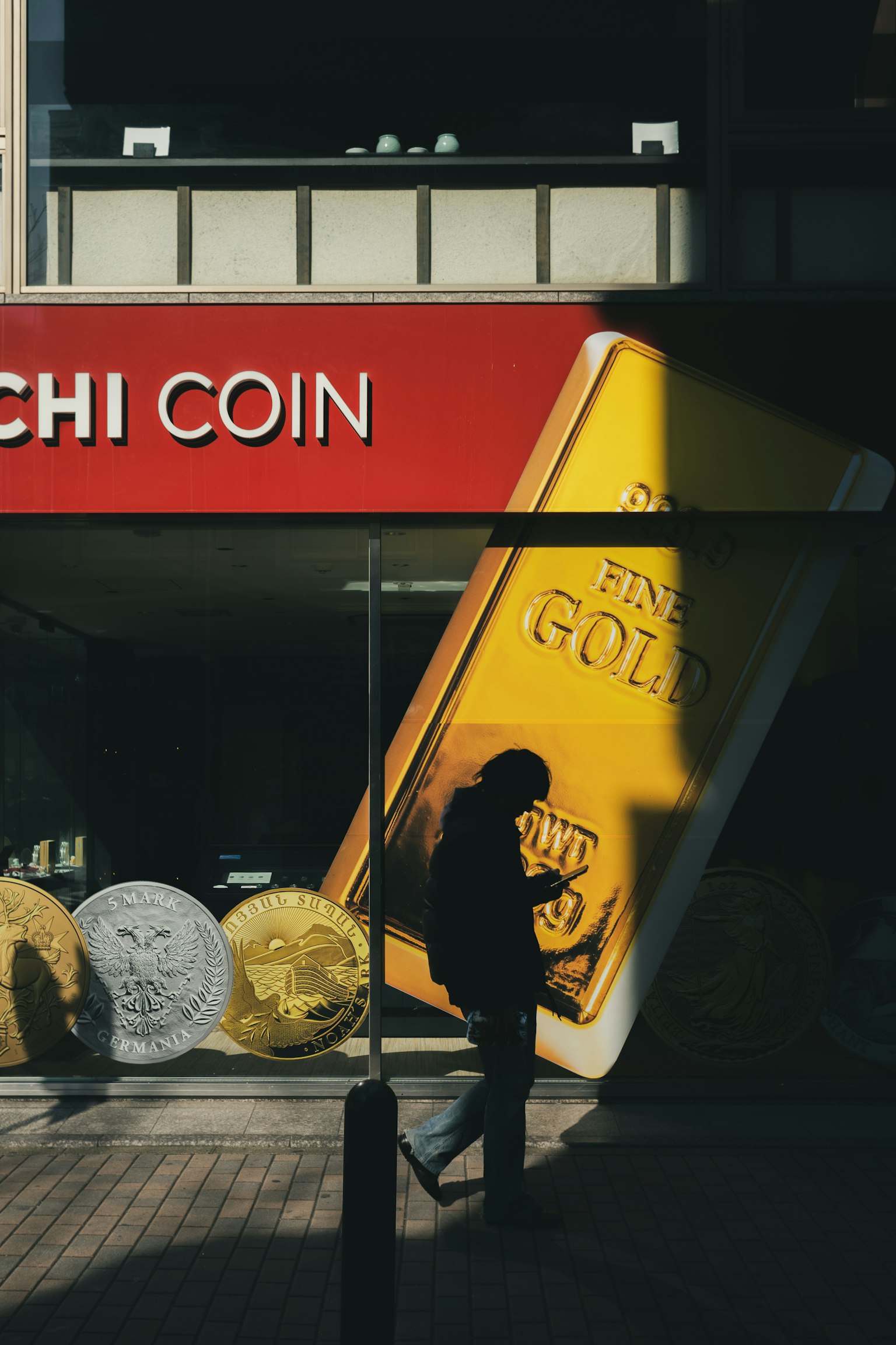 Silhouette of a person walking in front of a red sign and a gold bar advertisement