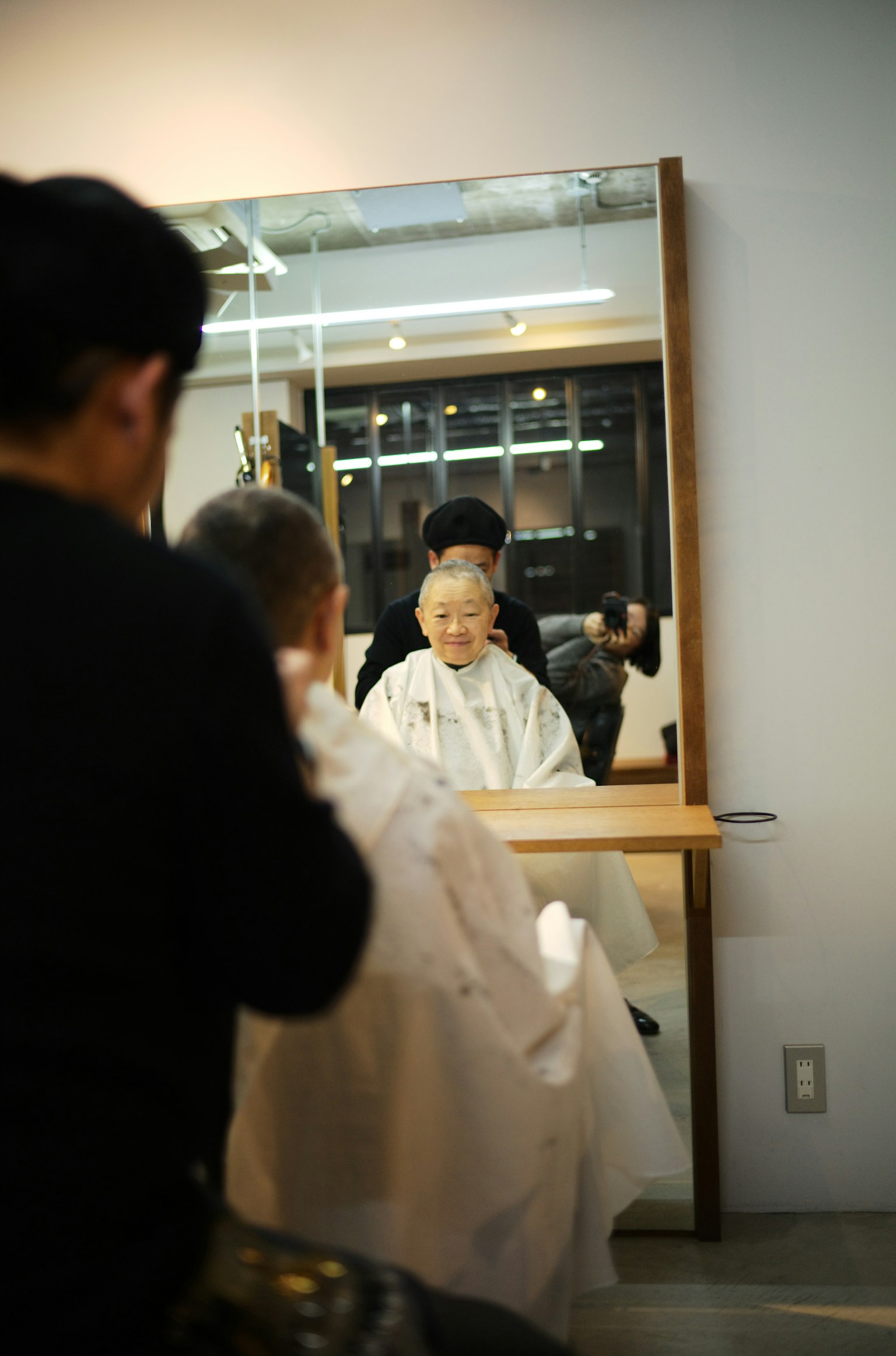 Femme âgée se faisant couper les cheveux dans un salon reflétée dans un miroir