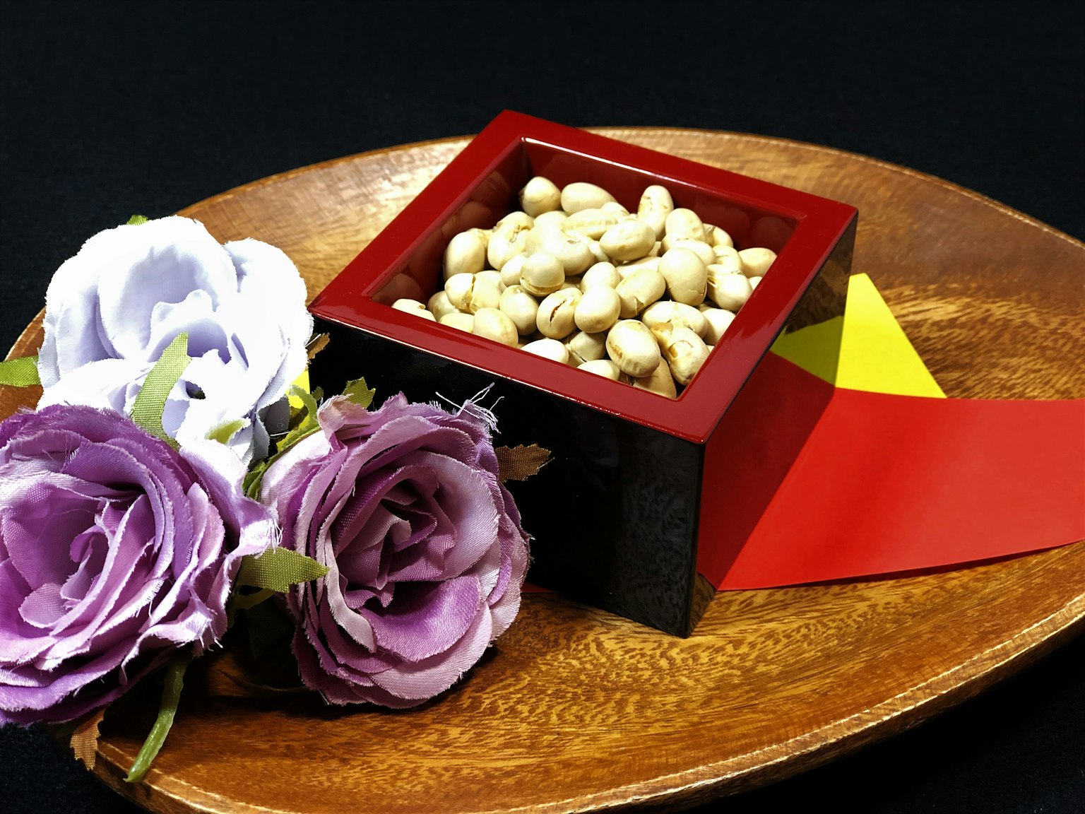 Un plato de madera con una caja roja llena de frijoles blancos y flores moradas