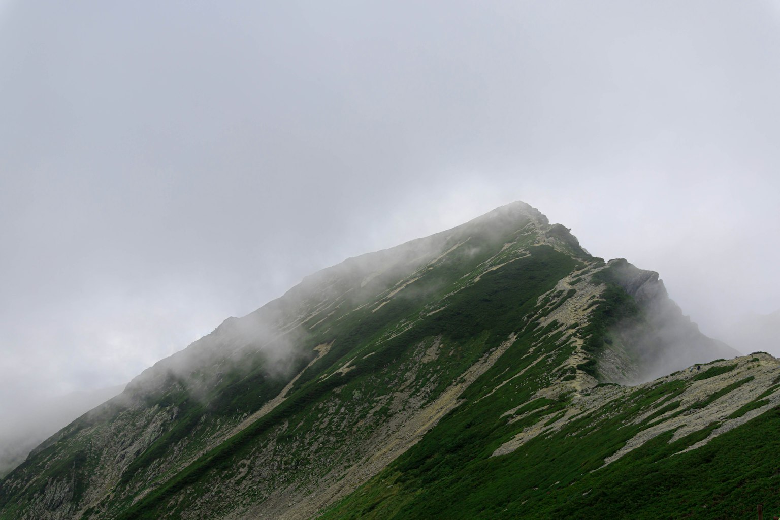 Picco di montagna avvolto nella nebbia con pendii verdi e cielo nuvoloso