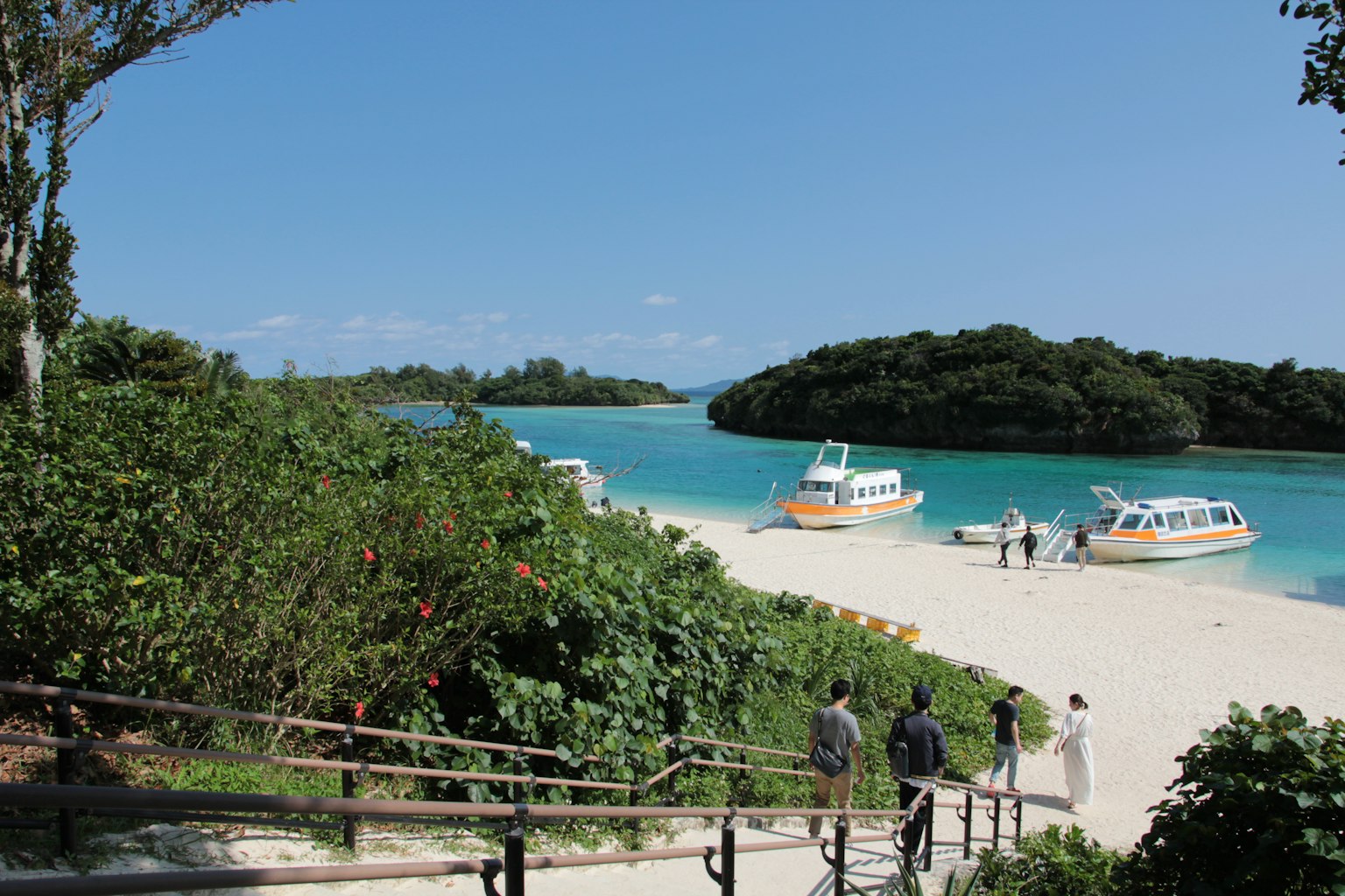 Vista panoramica di barche su un mare blu con spiaggia di sabbia bianca e vegetazione lussureggiante