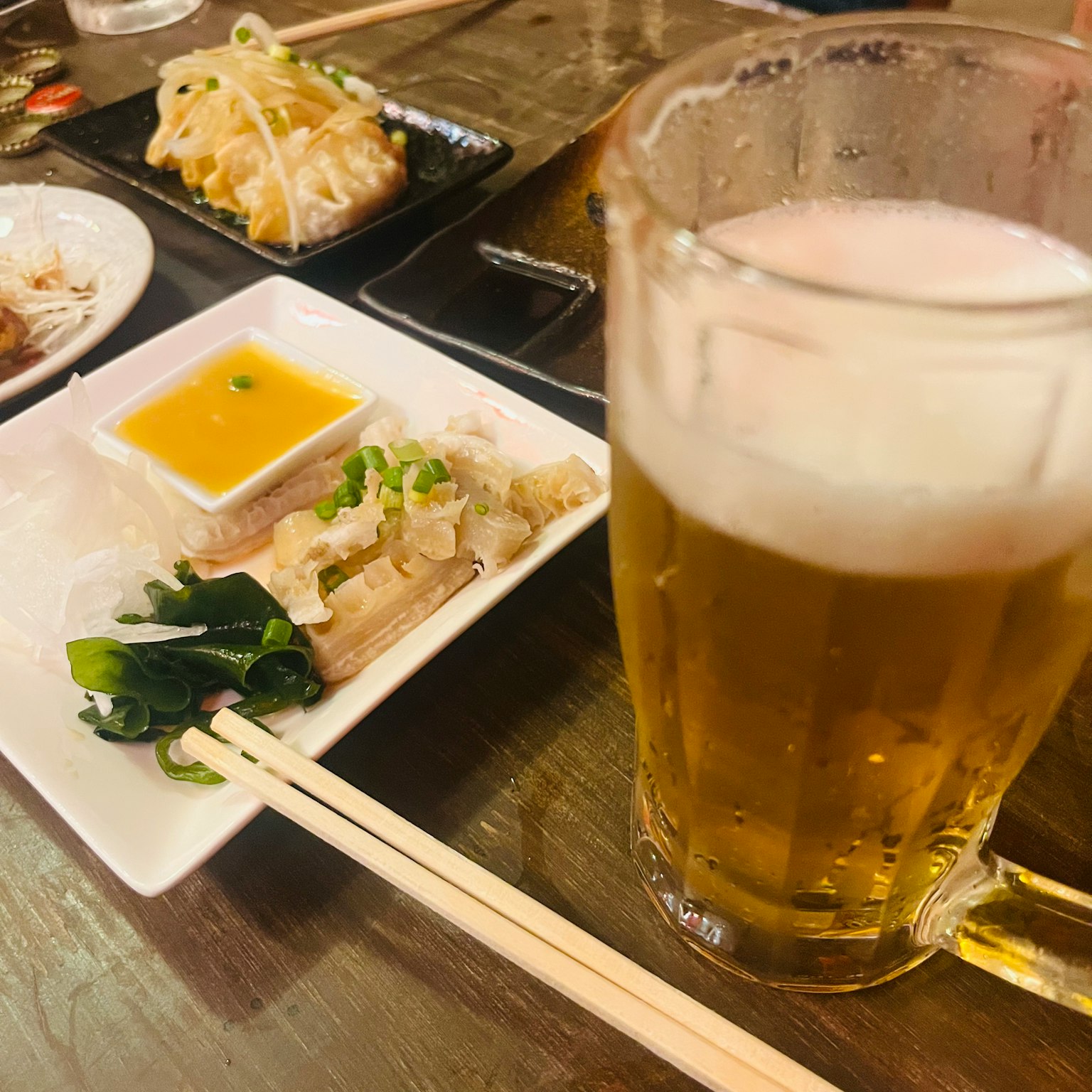 Un vaso de cerveza junto a un plato de aperitivos en una mesa