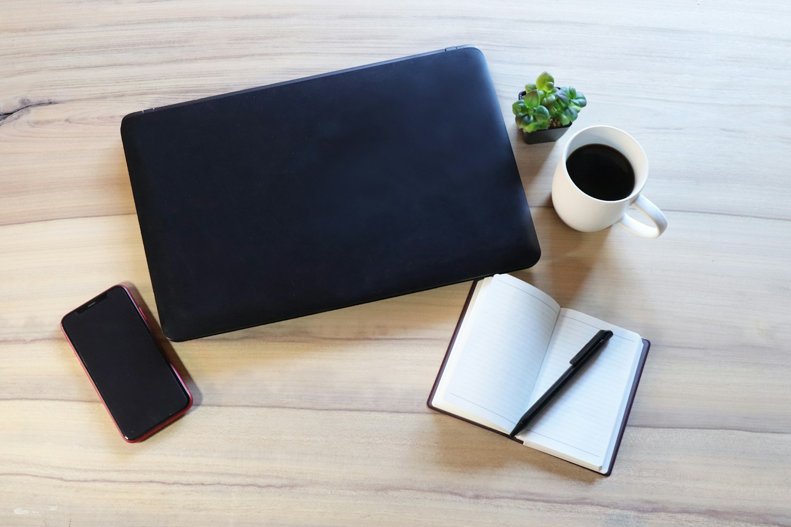 schwarzes laptop und weiße tasse auf einem holztisch mit einem notizbuch und einem smartphone