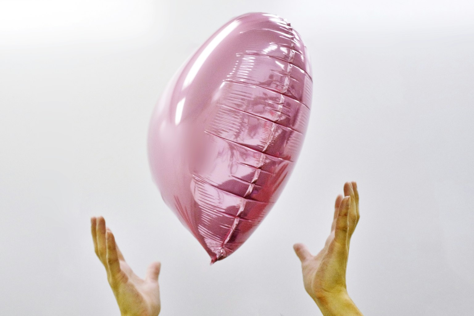 A pink heart-shaped balloon floating above two hands