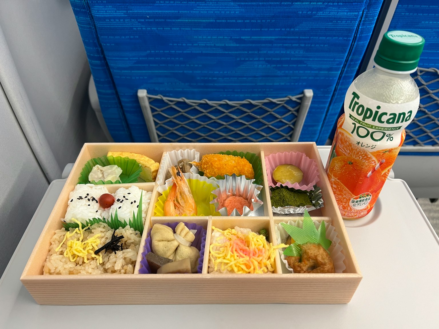 Une boîte à bento magnifiquement arrangée sur un plateau d'avion avec du jus Tropicana