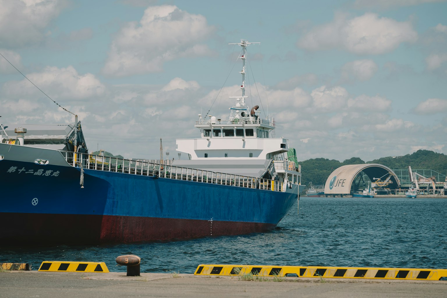 Navire de marchandises bleu amarré au port sous un ciel nuageux