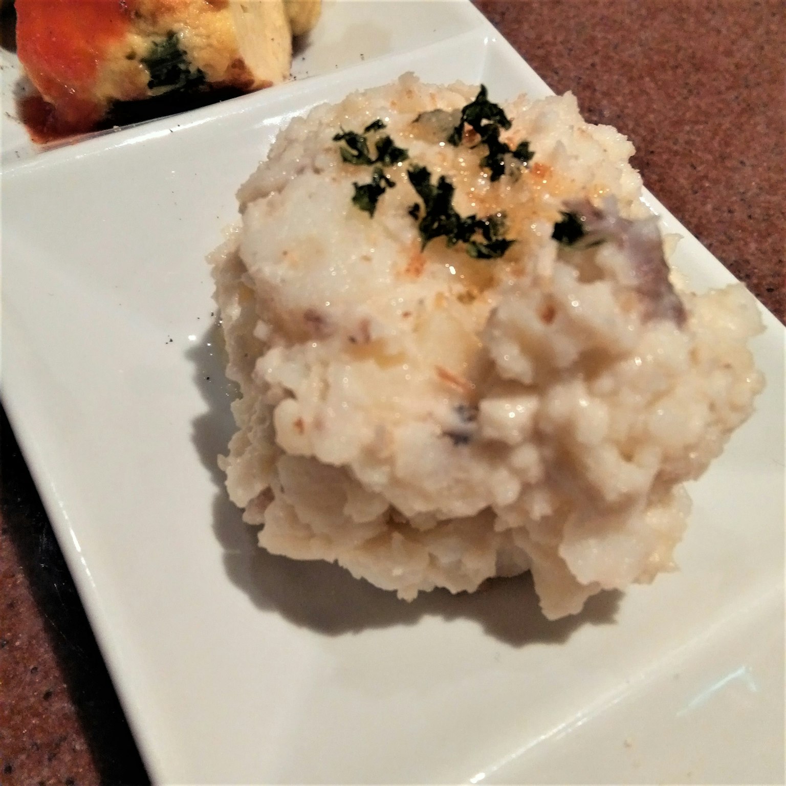 Creamy mashed potatoes topped with parsley served on a square plate
