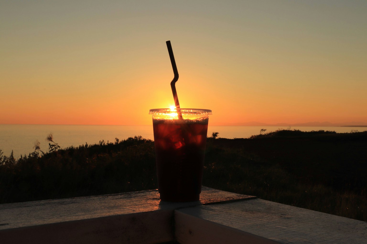 Vaso de café helado contra un atardecer