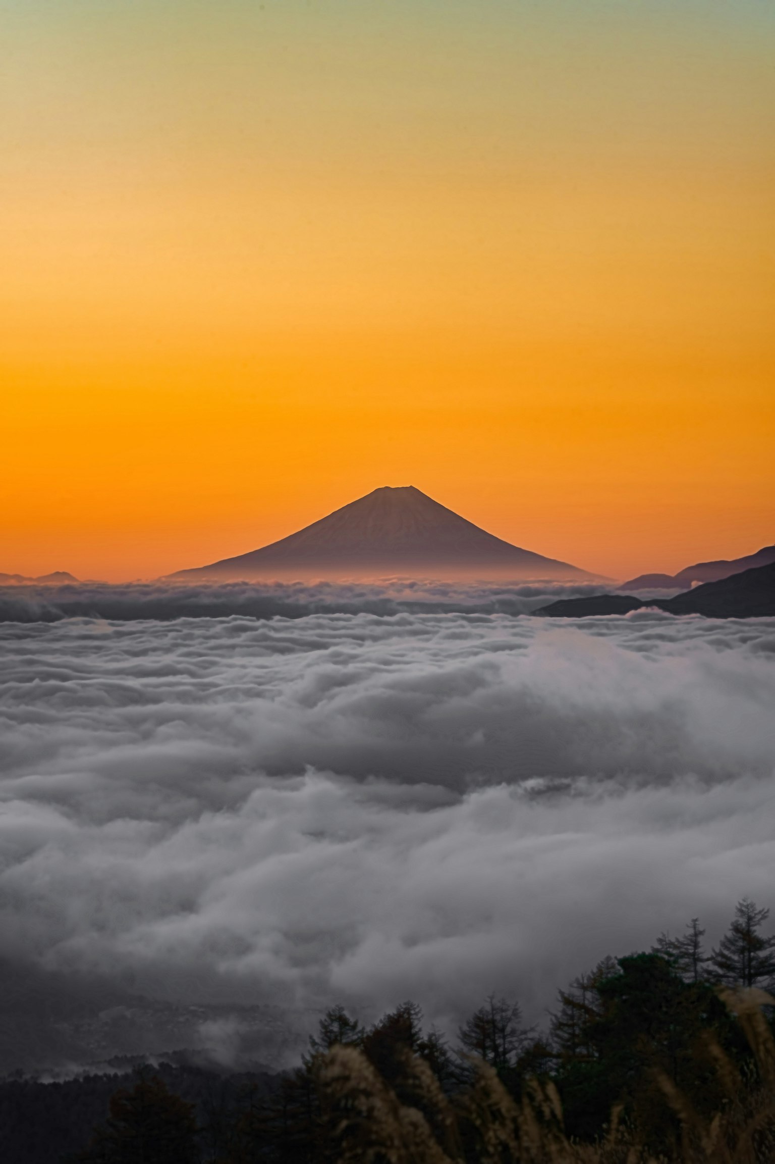 Silhouette di una montagna che emerge sopra un mare di nuvole durante un bel tramonto