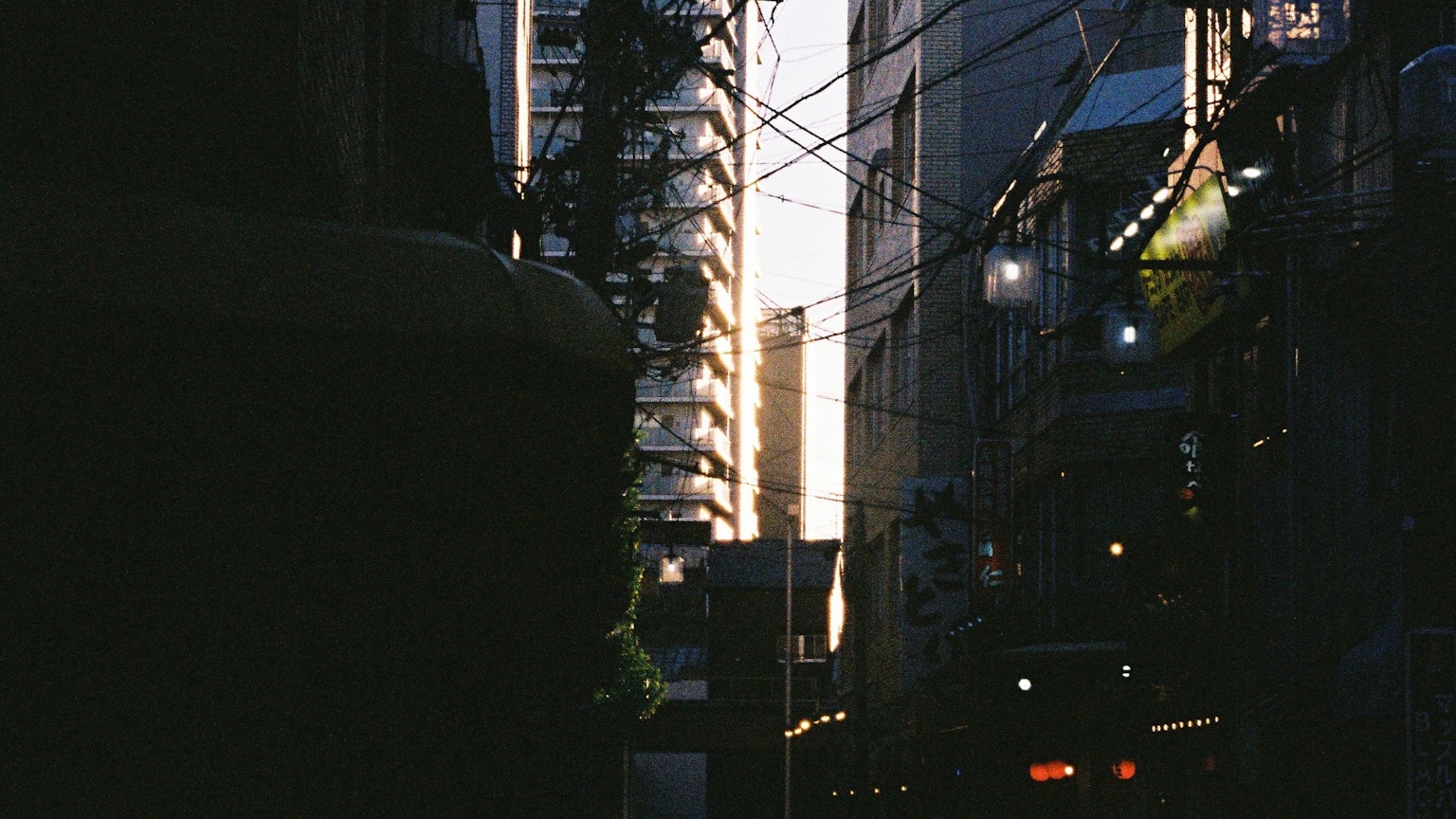 Narrow urban alley at dusk with high-rise buildings and power lines