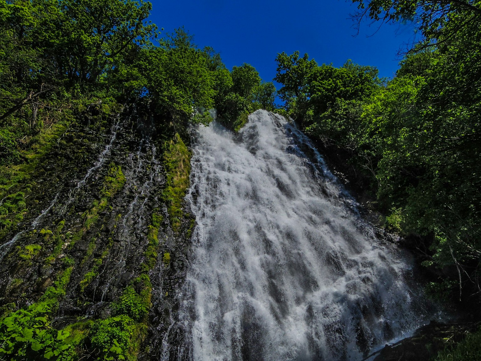 Una hermosa cascada rodeada de exuberante vegetación con un cielo azul claro