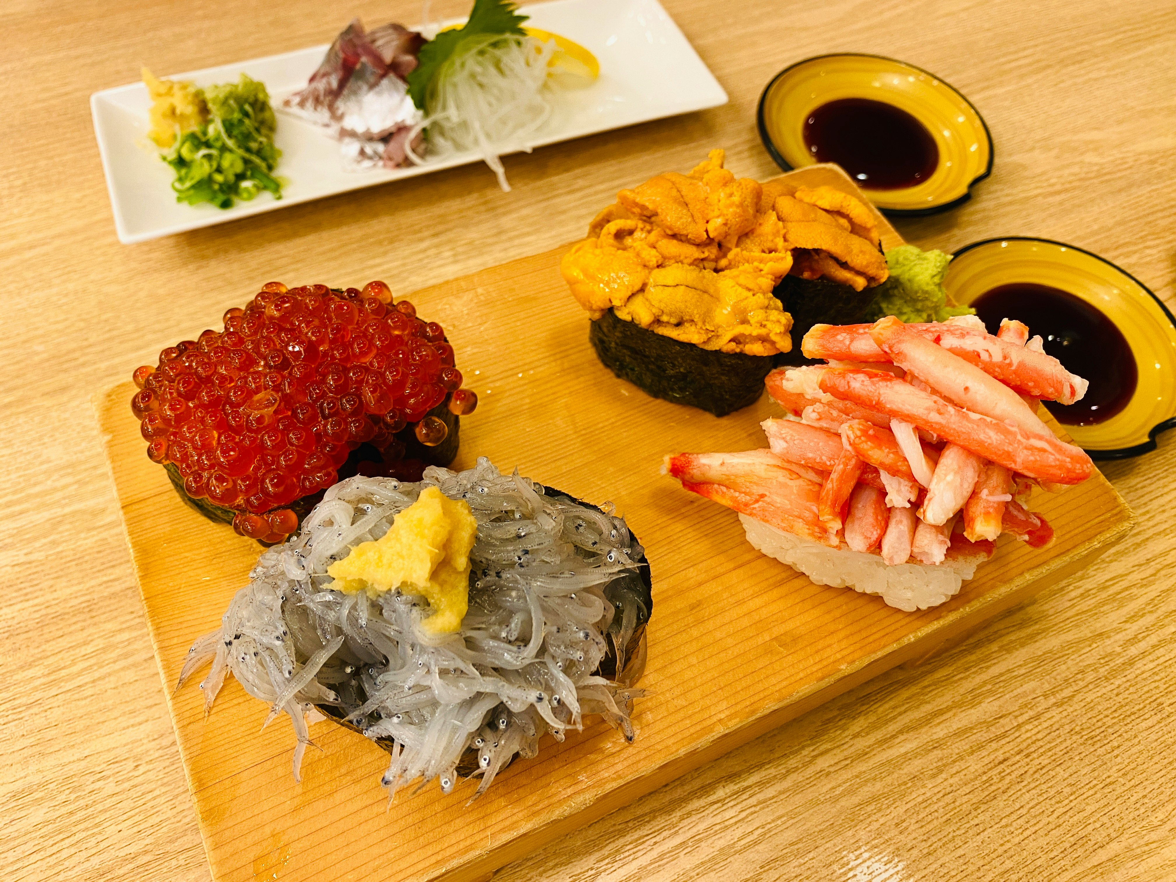 aneka topping sushi dan saus bumbu tersusun di atas talenan kayu