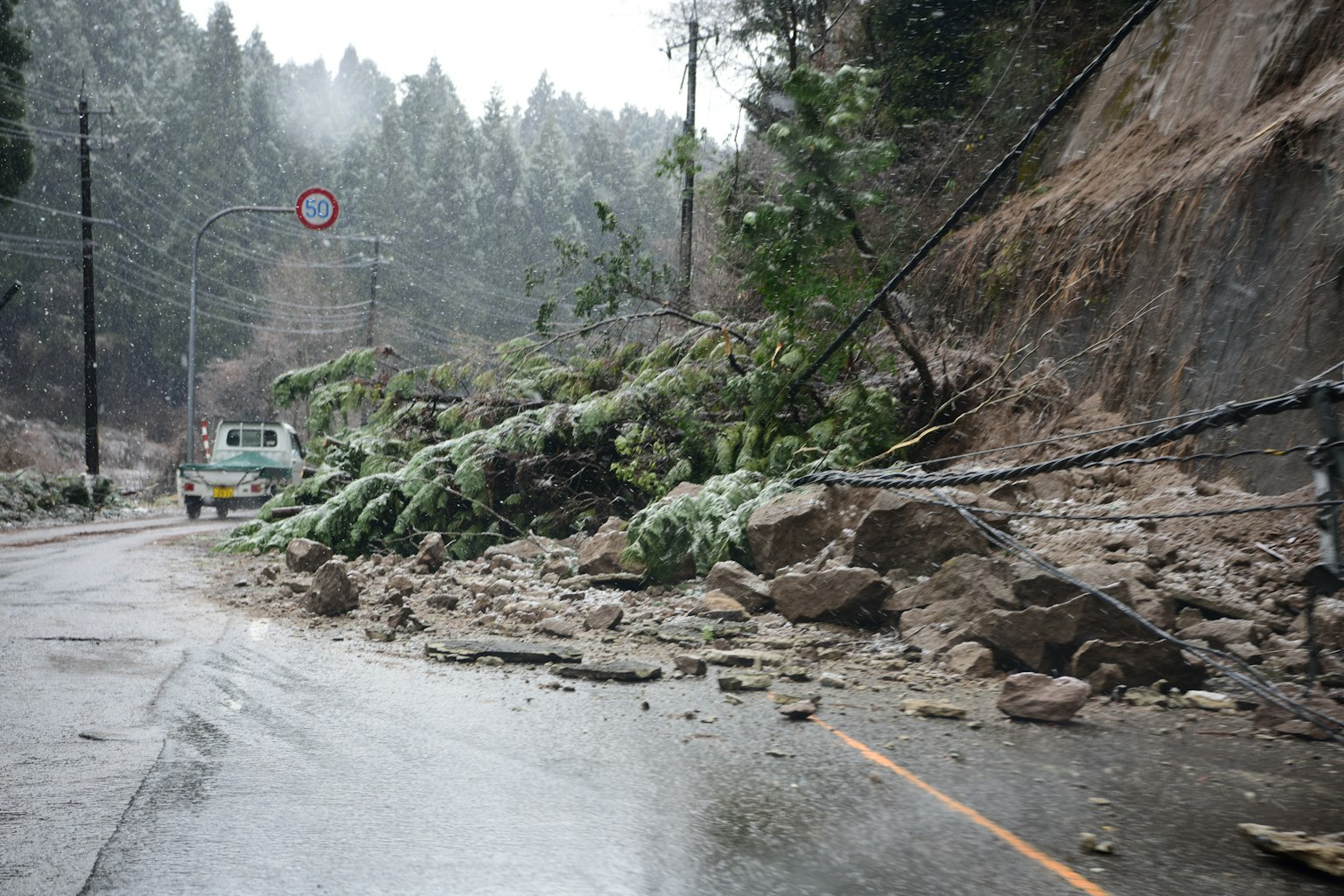 Landslide blocking the road with wet pavement and fallen trees