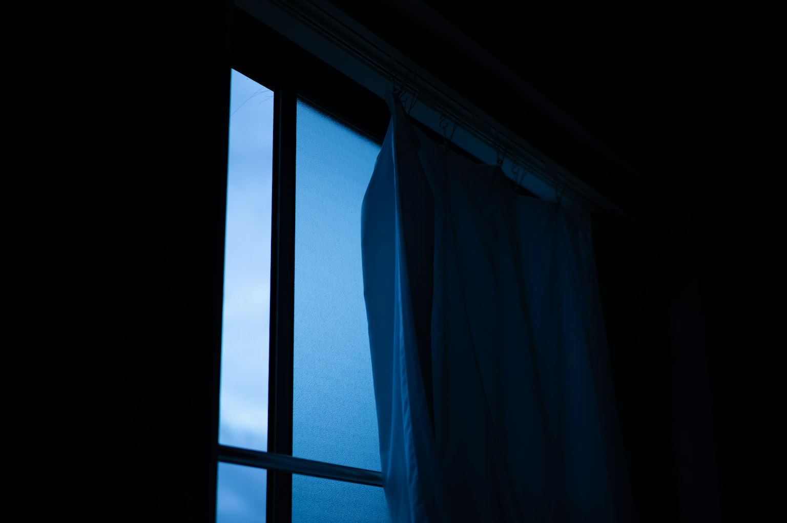 Silhouette di una finestra con luce blu e tendina bianca