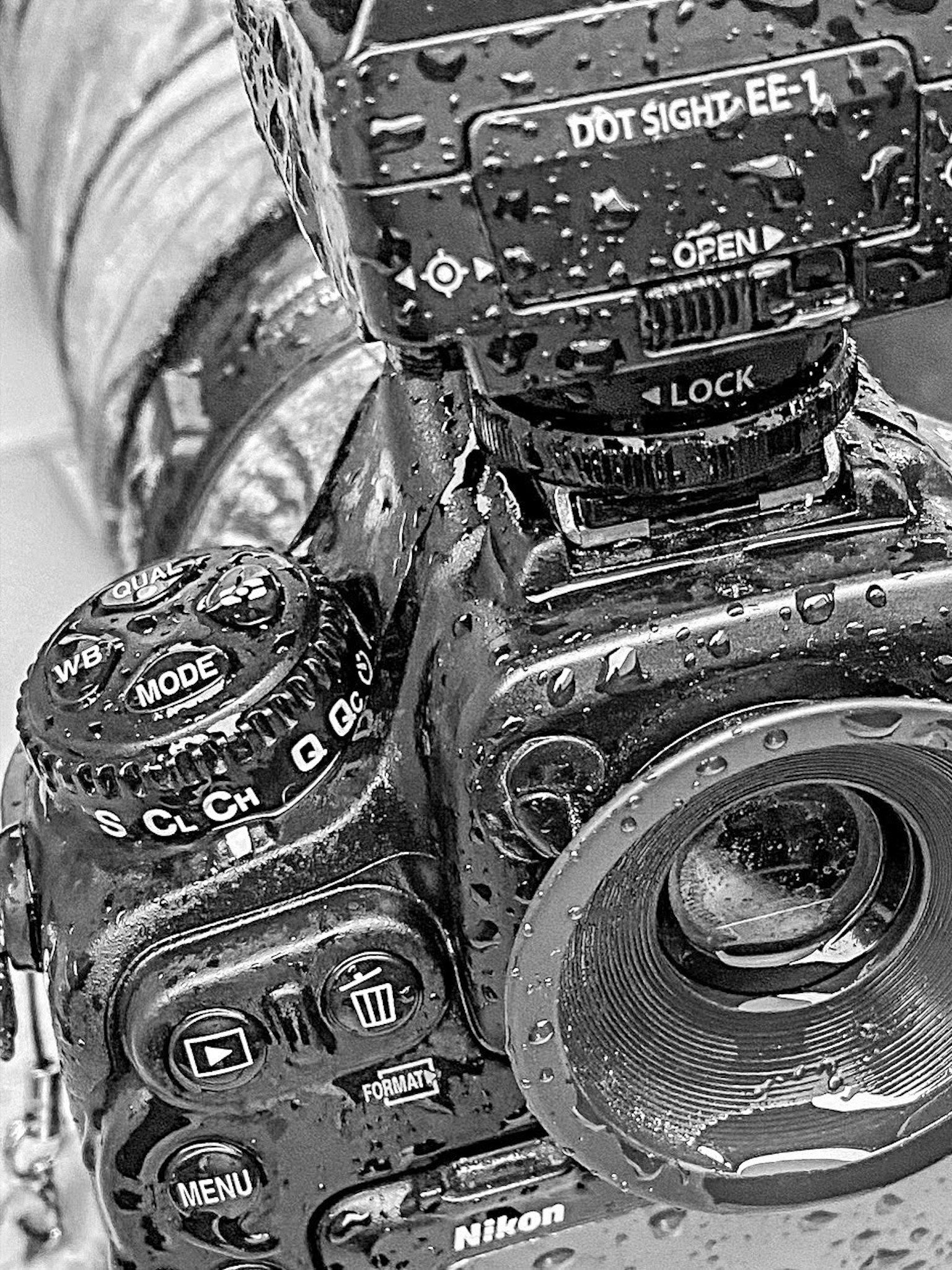 Primo piano di una fotocamera Nikon bagnata che mostra vari pulsanti e dettagli dell'obiettivo