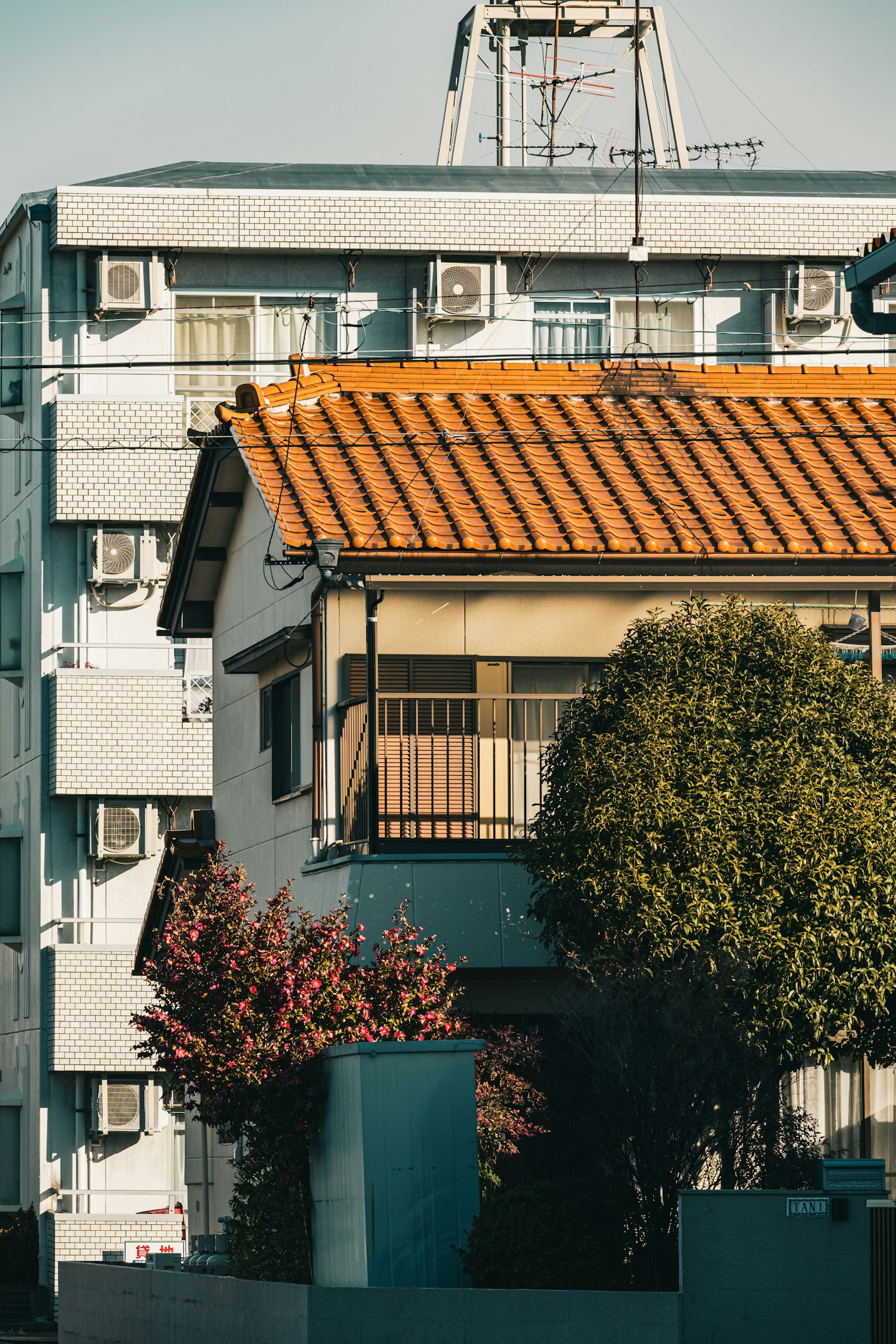 Una casa con un techo naranja junto a un edificio con unidades de aire acondicionado y árboles en flor