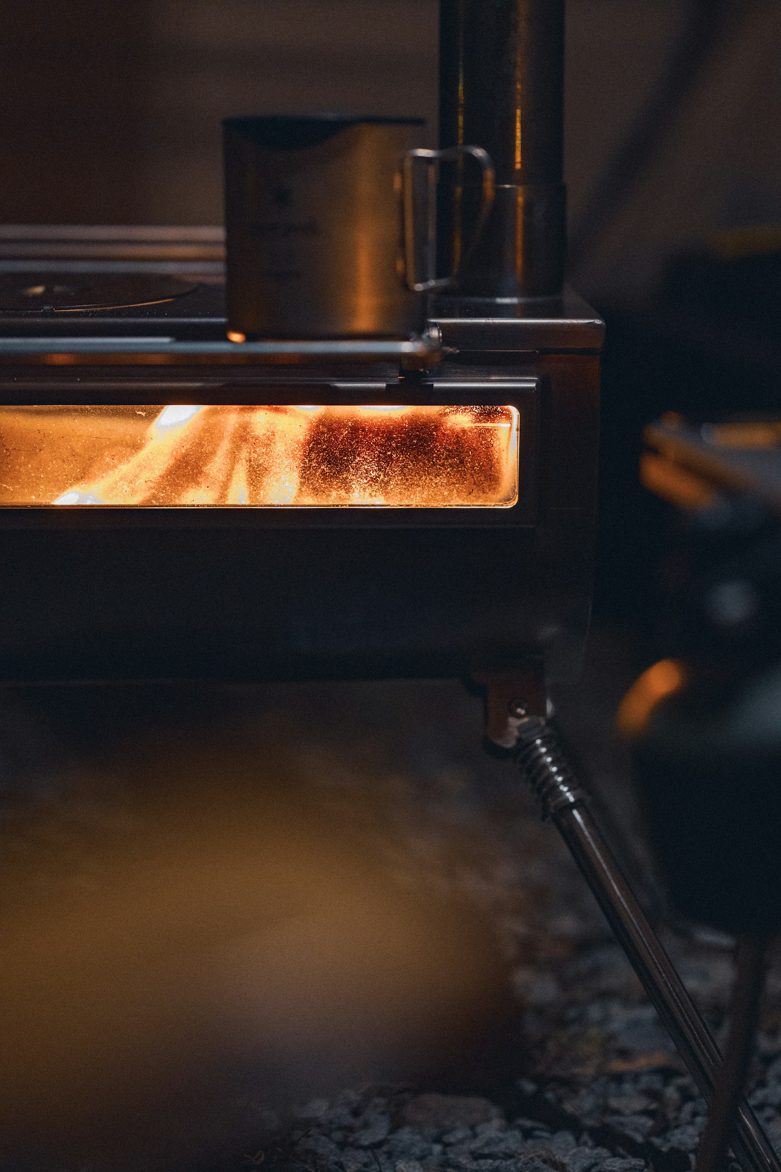 暖炉の近くで燃える木材と金属製のマグカップが映る