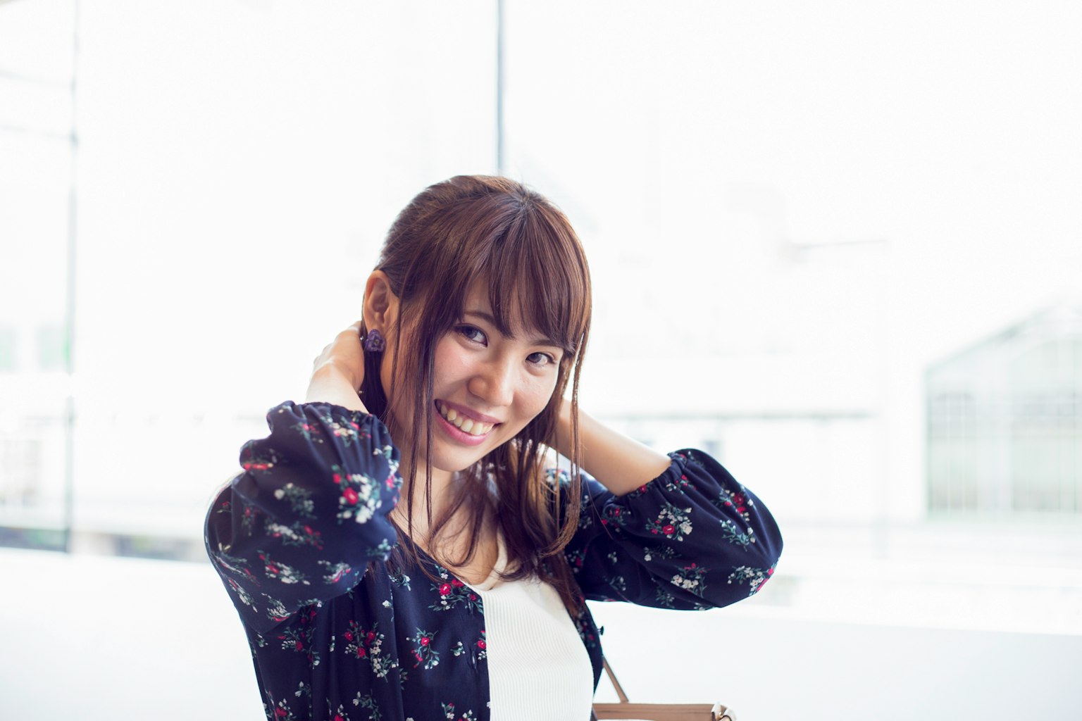 Smiling woman adjusting her hair near a bright window