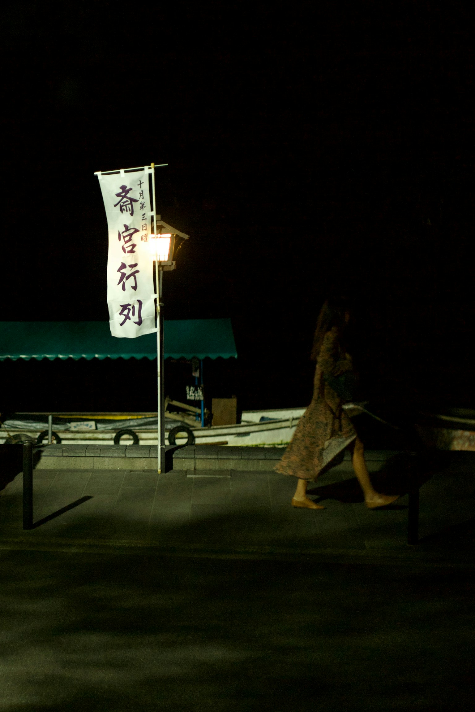 夜の港で旗がはためく中を歩く女性