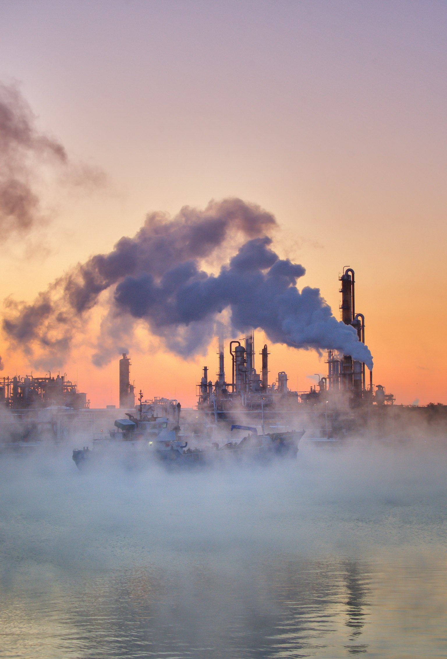 Usine émettant de la fumée avec un reflet de coucher de soleil sur l'eau