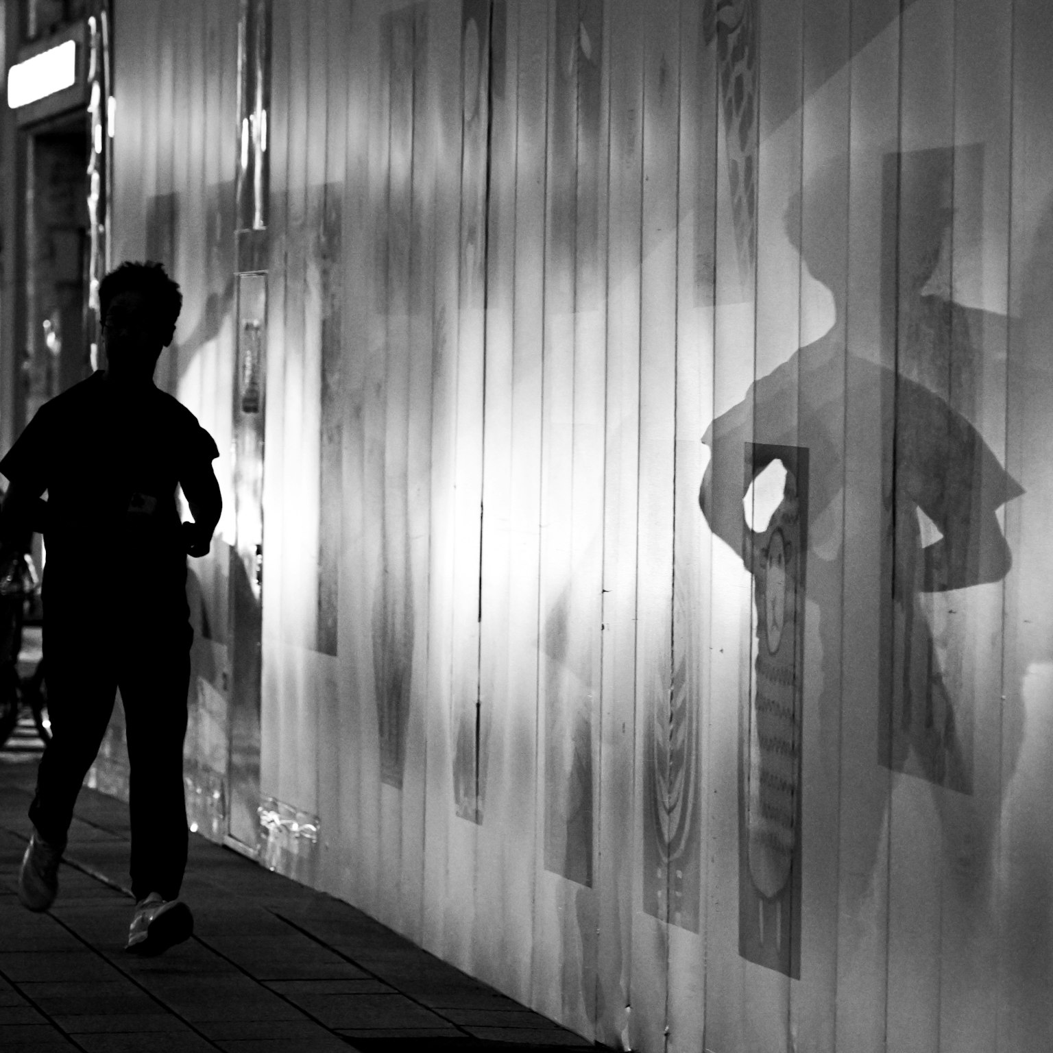 Bóng silhouette của một đứa trẻ đang chạy dọc theo bức tường với bóng đổ tương phản trong đen trắng