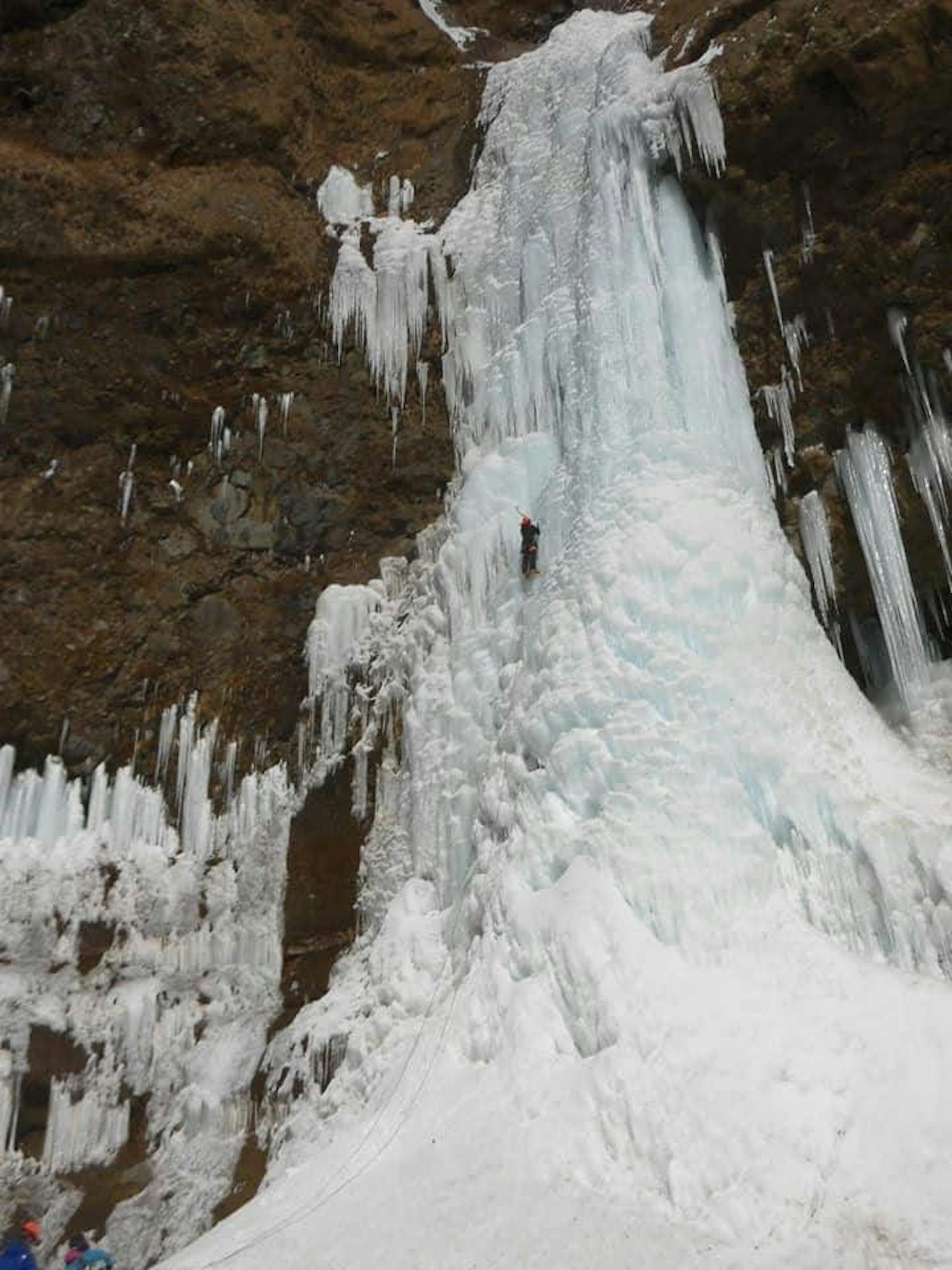 Air terjun beku dengan pendaki es yang mendaki permukaan es