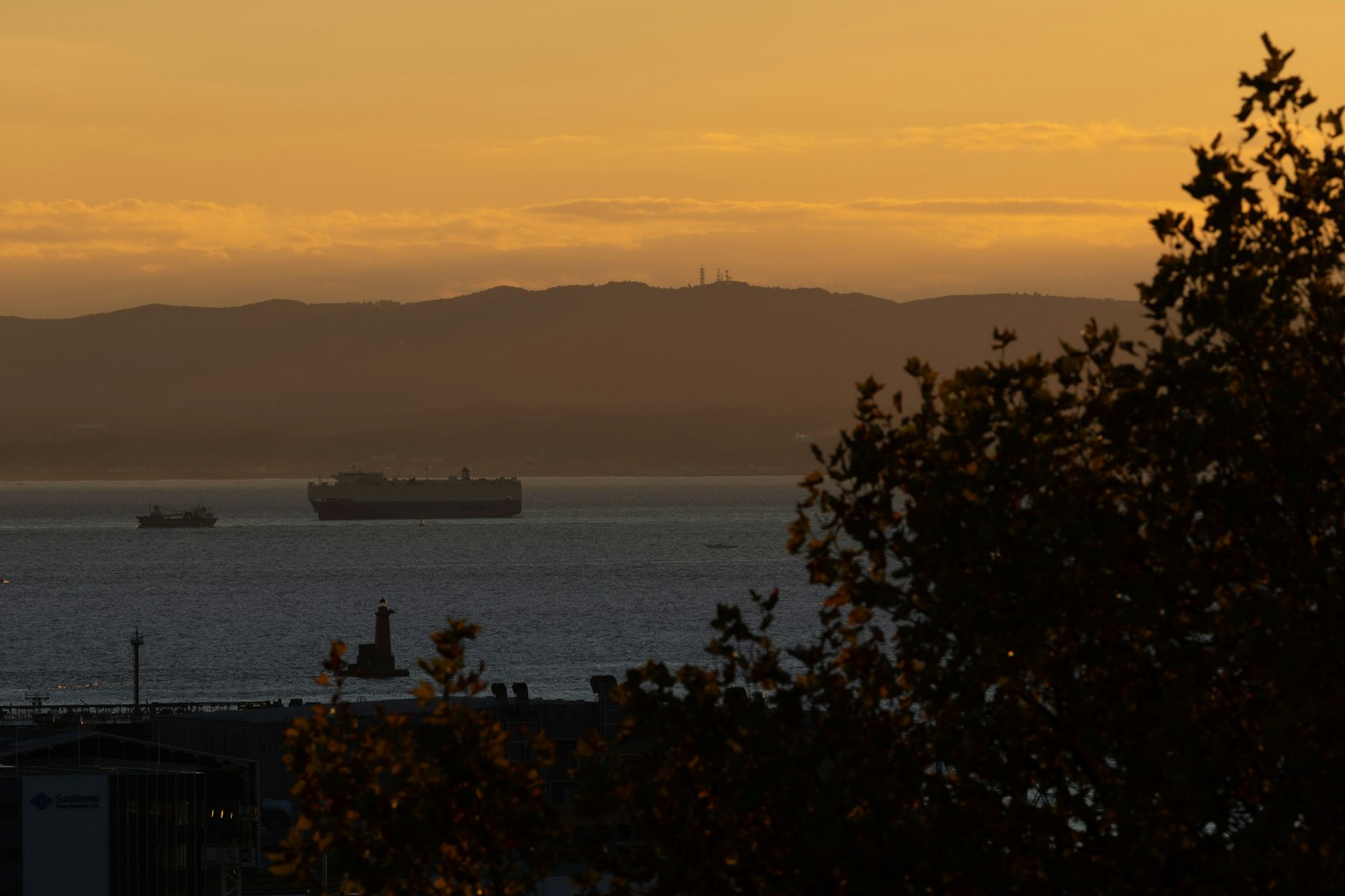 Barcos de carga en el océano al atardecer con montañas en silueta