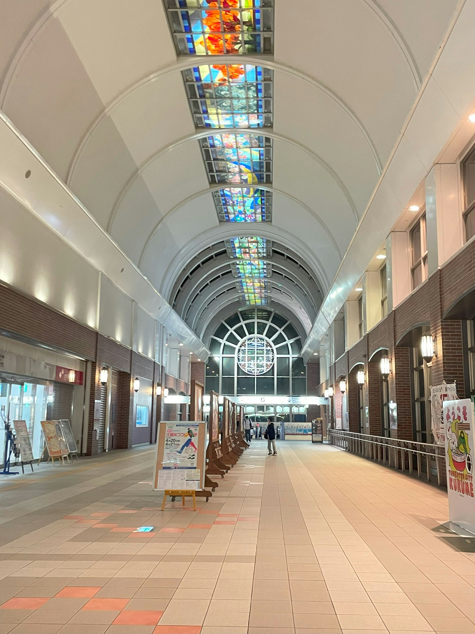 Amplio y moderno interior de un edificio con una arcade brillante Hermosas ventanas de vidrio de colores adornan el techo Personas caminando por el pasillo