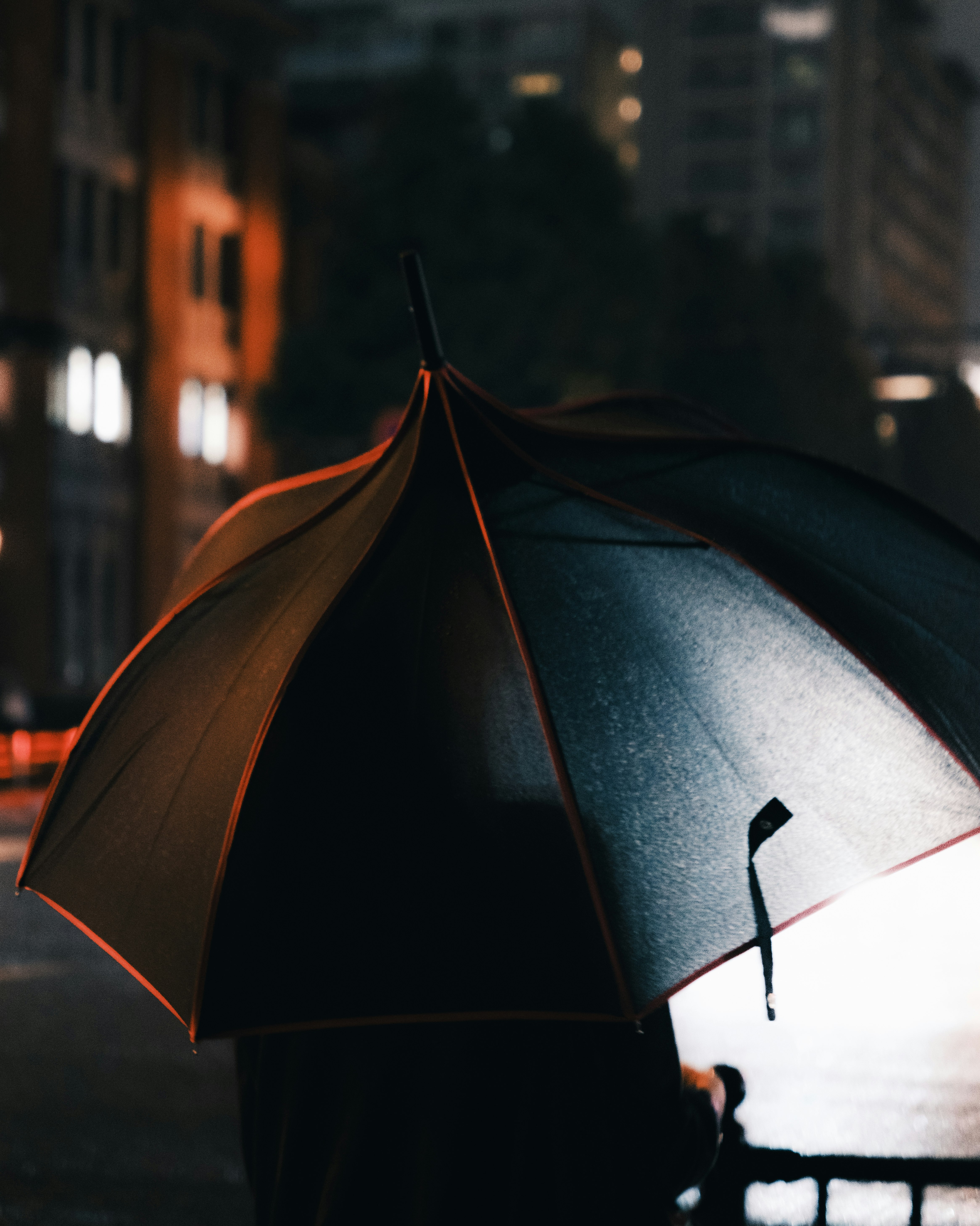 Rückenansicht einer Person mit Regenschirm in einer Nachtstadt