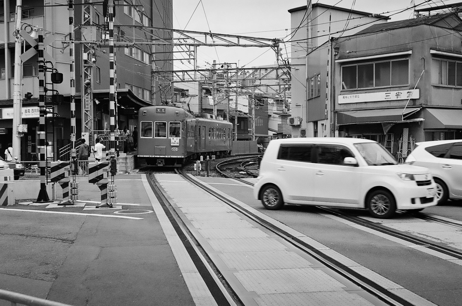 Scena in bianco e nero di un treno e un'auto che si incrociano all'angolo di una strada