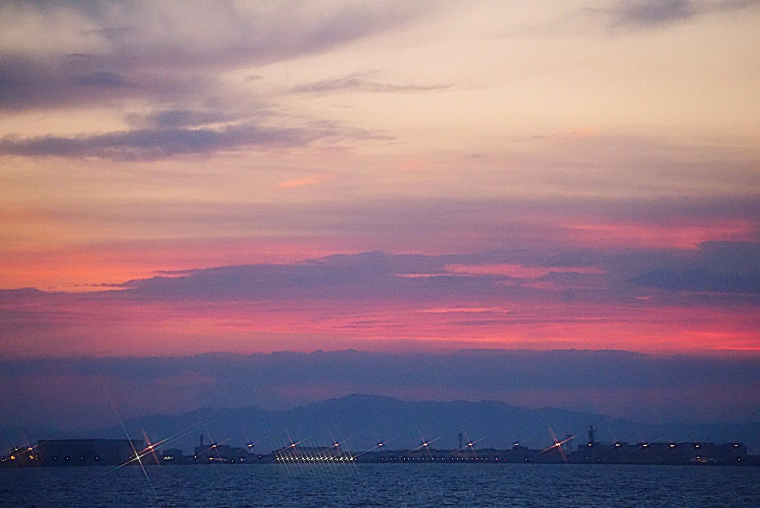 Tramonto sul mare con luci di un porto