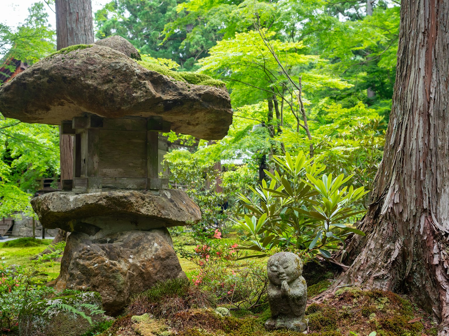 Lanterna di pietra e piccola scultura in un giardino lussureggiante