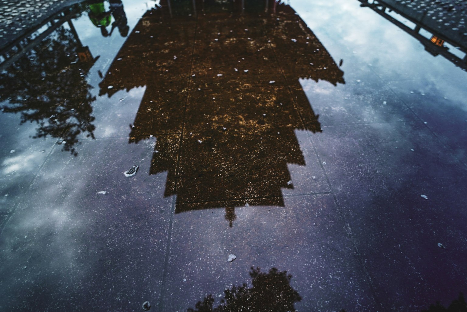 Reflection of a building in a puddle with clouds above
