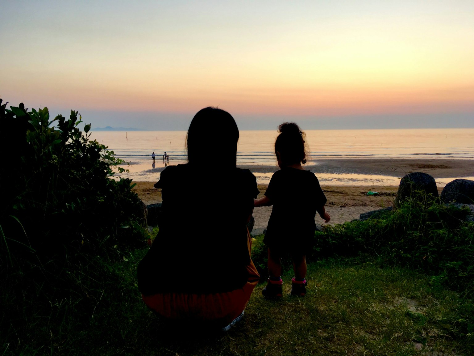 夕日を背景に海を見つめる母親と子供のシルエット
