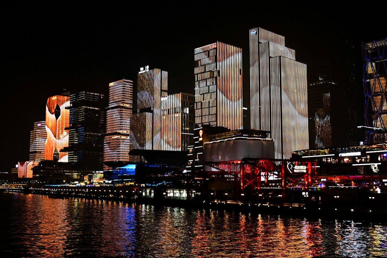 夜の都市のビル群に映し出されたカラフルなプロジェクションと水面に映る光