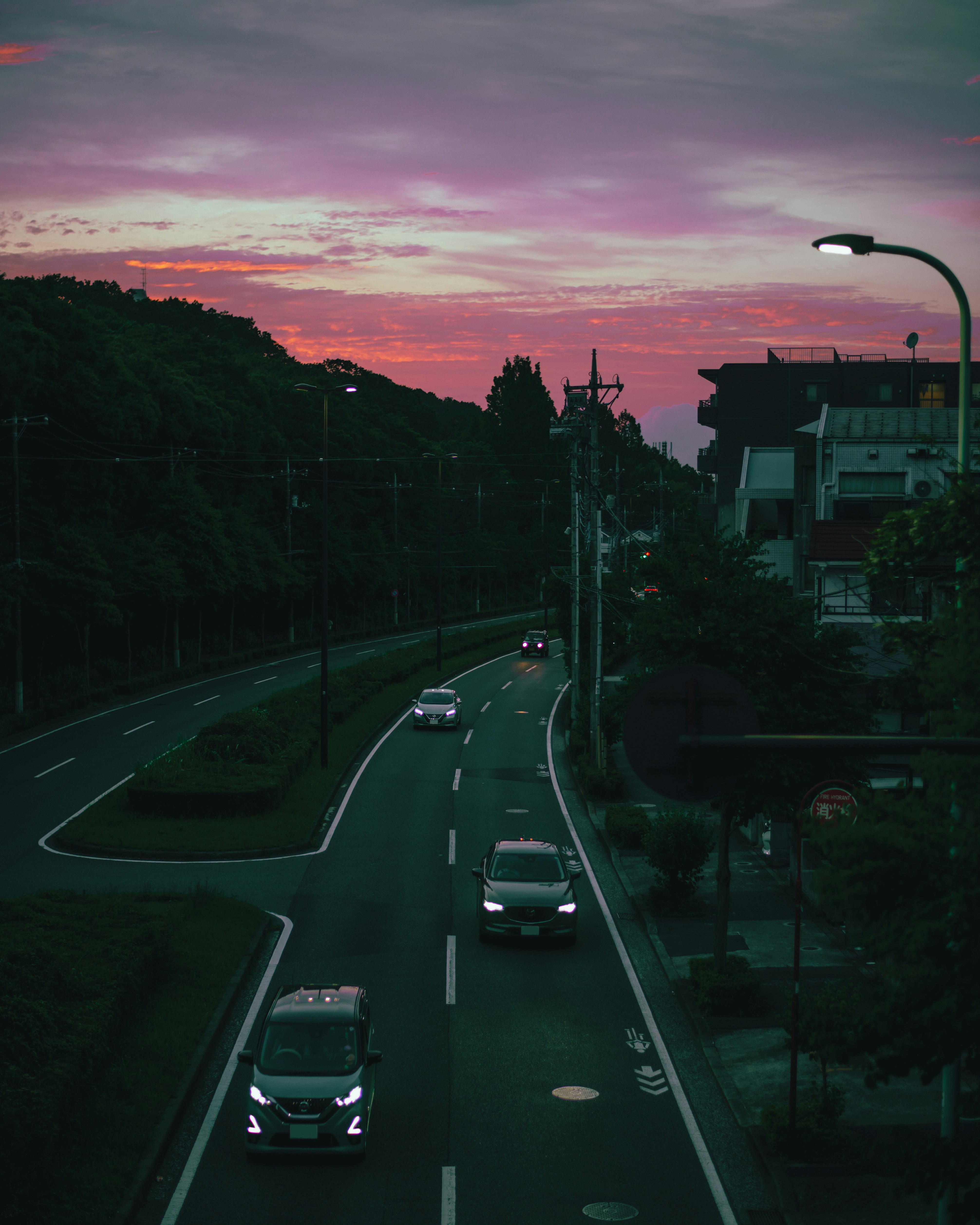 夕暮れの郊外道路を走る車と街並み