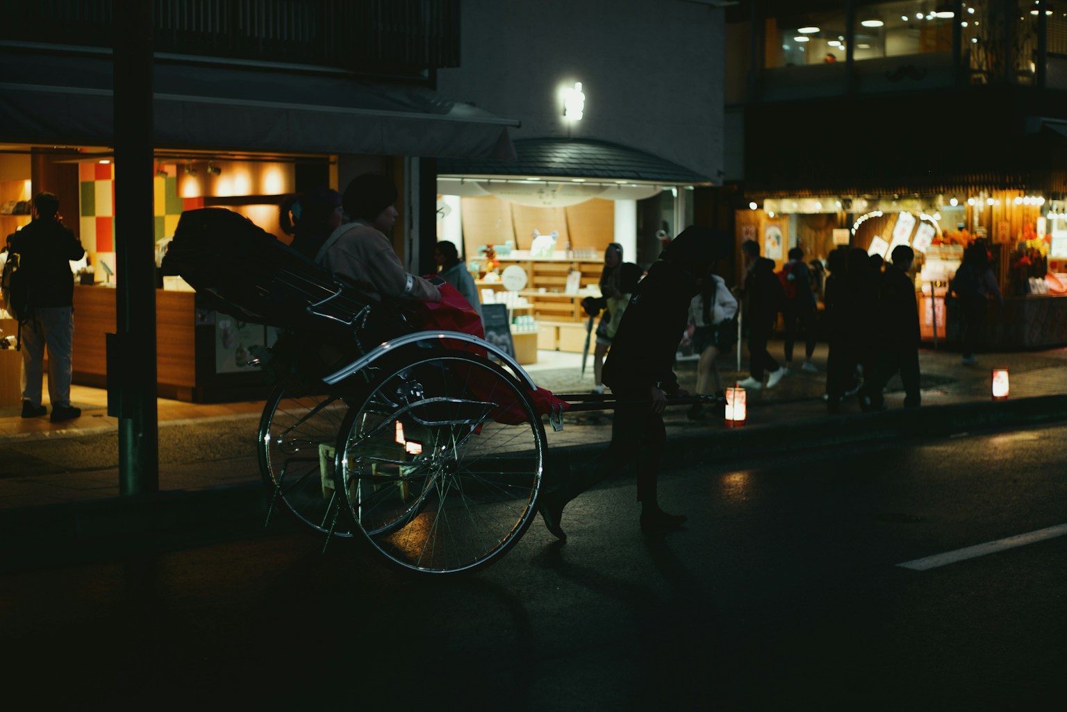 A rickshaw moving through a nighttime street with shop lights in the background