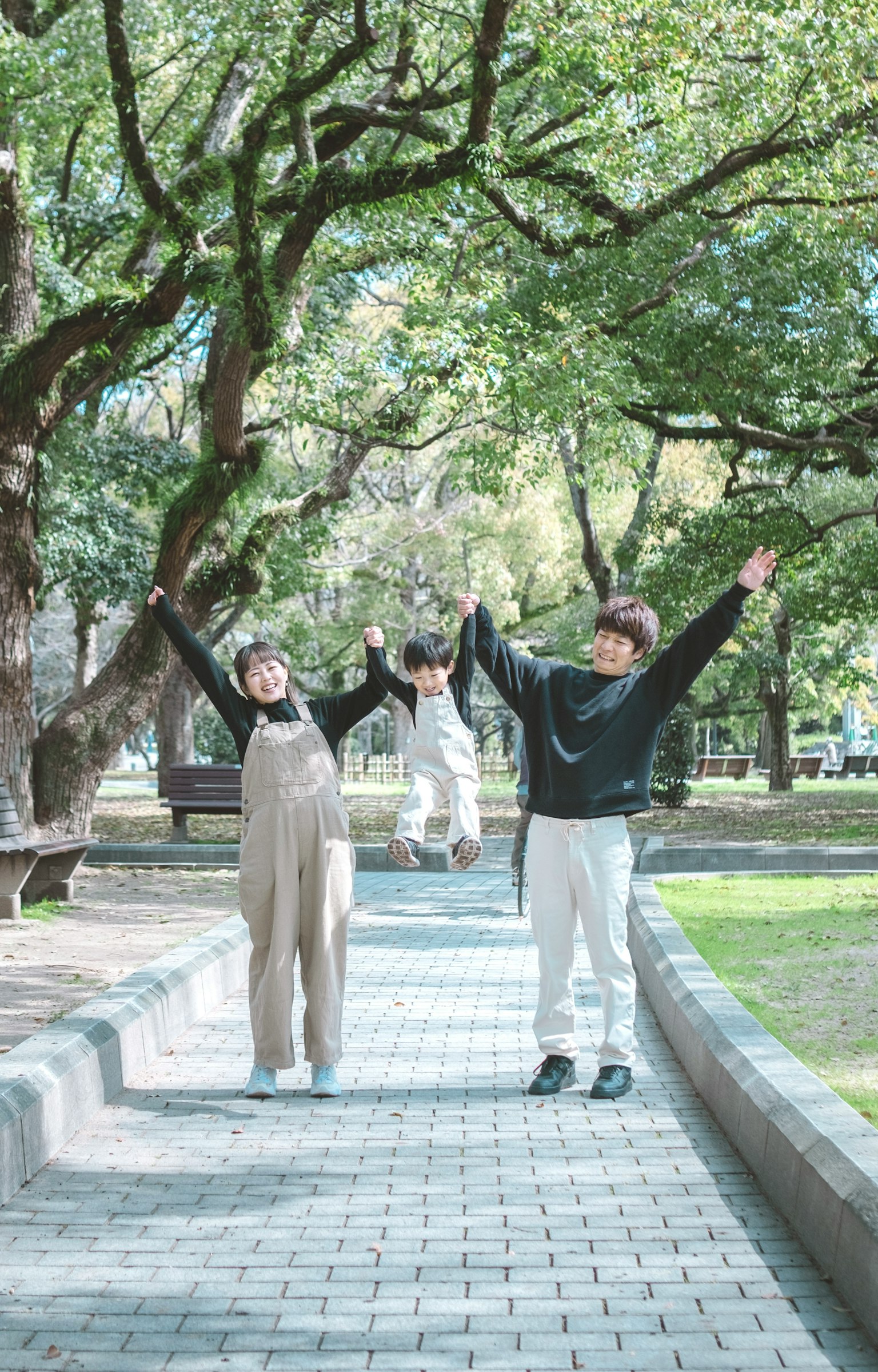 Deux jeunes levant les mains joyeusement dans un parc avec une troisième personne derrière eux entourée d'arbres verts