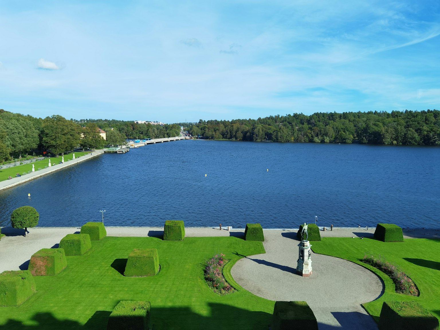 Vista de un lago rodeado de hierba verde y una estatua