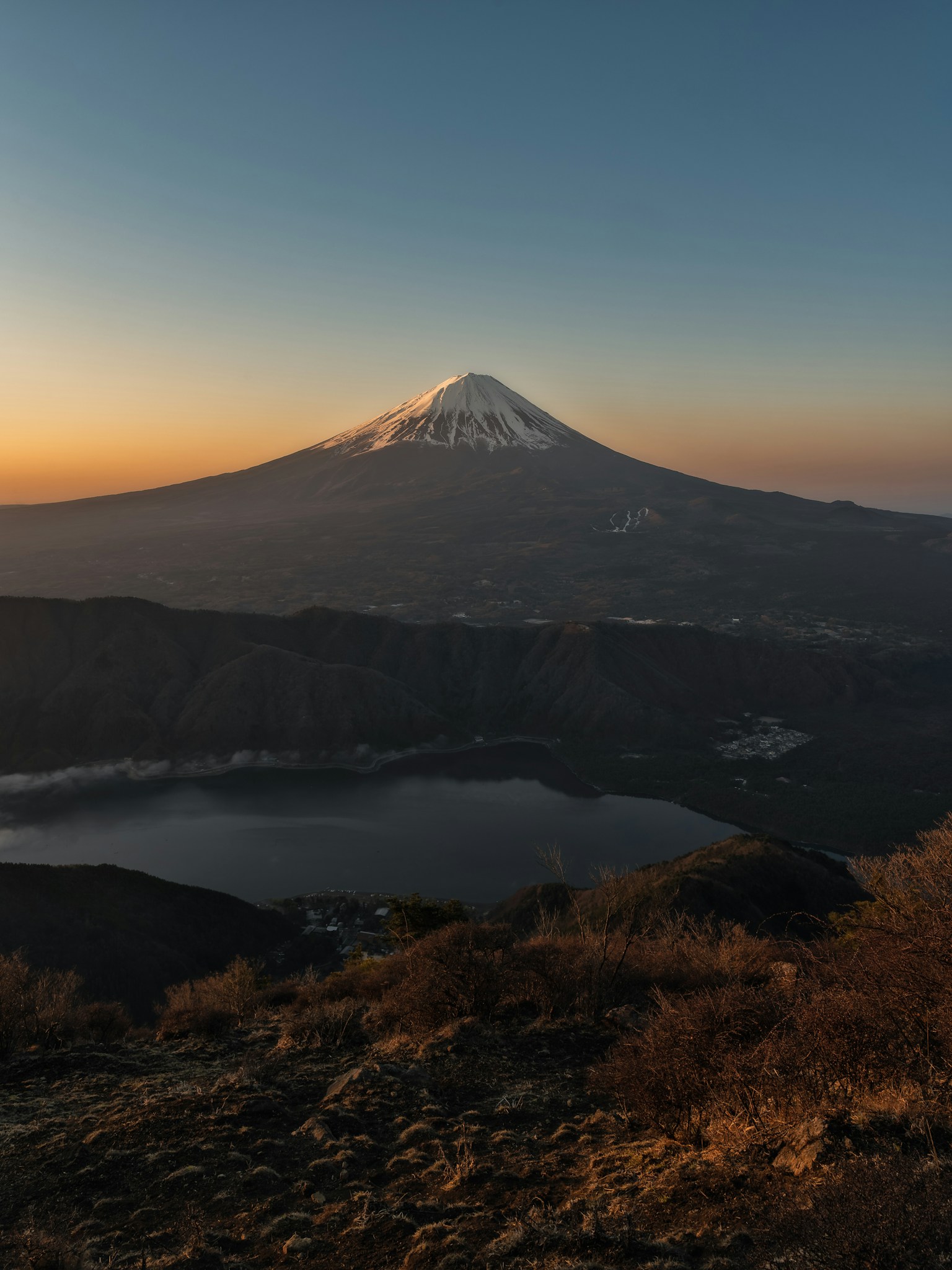 Monte Fuji innevato al tramonto con un lago sereno in primo piano