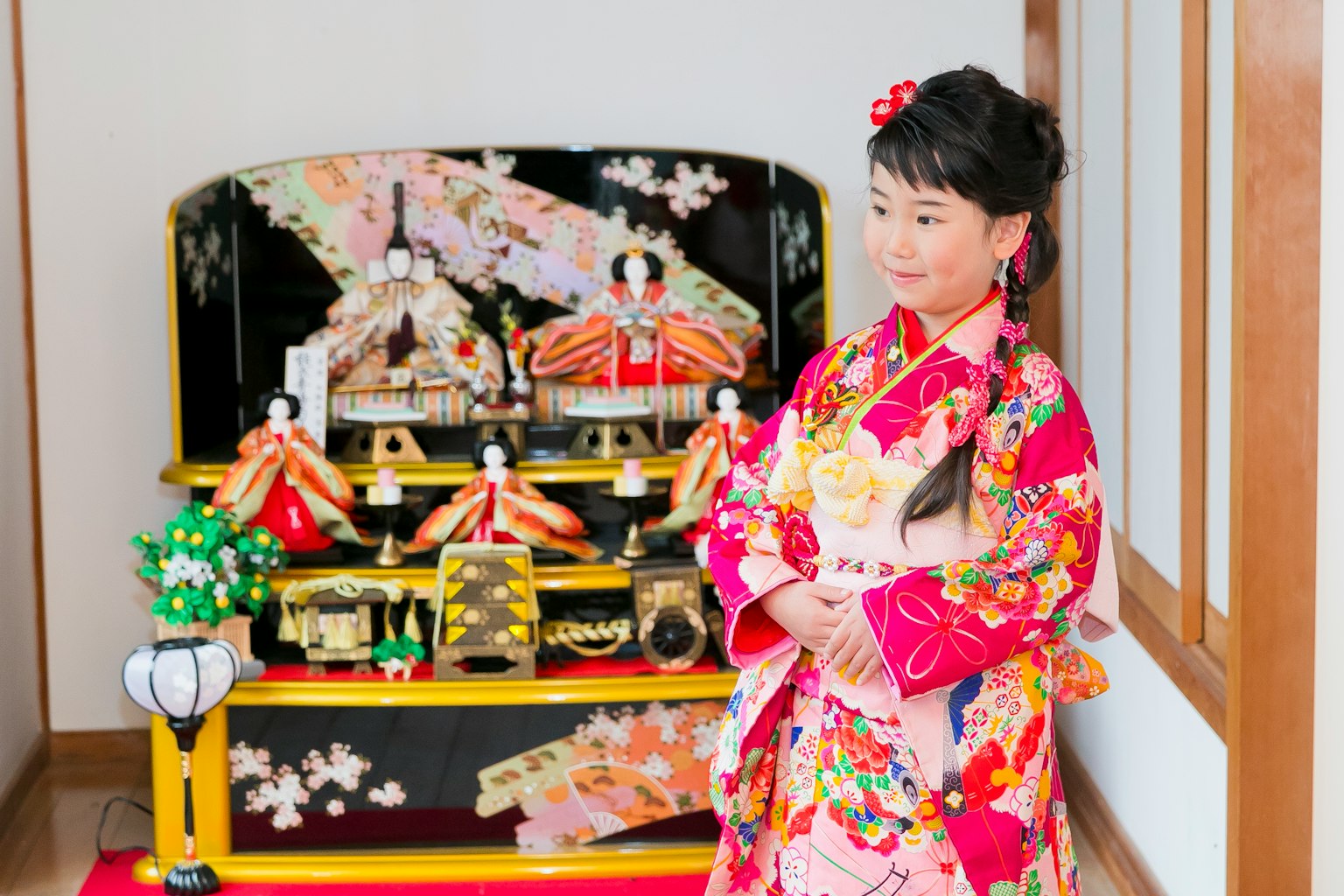 Une fille en kimono coloré pose devant des poupées hina