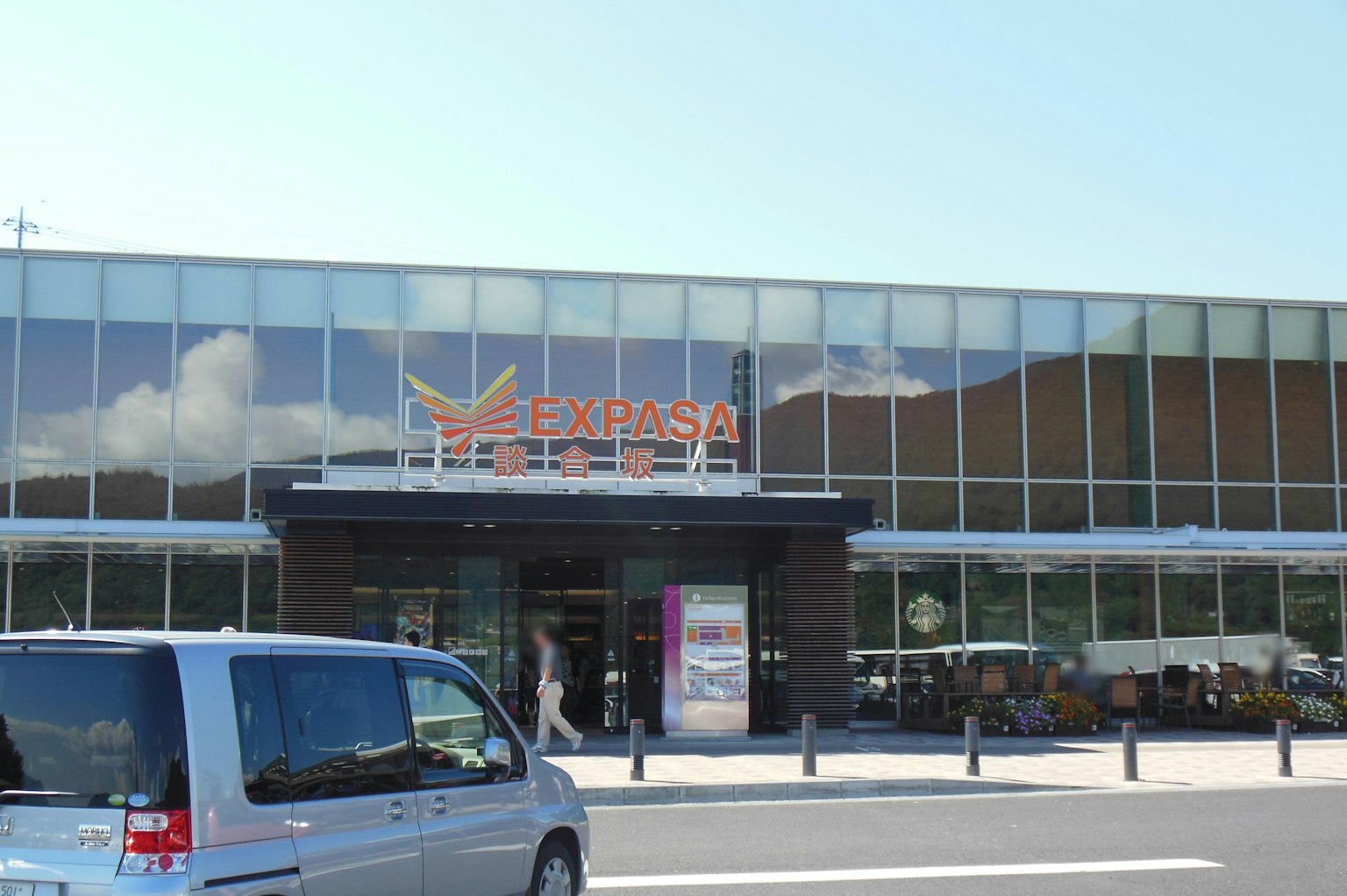 明亮天空下的Ekiparesa酒店现代外观，前面停着一辆车