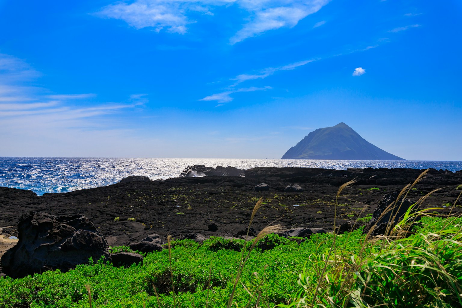 Pemandangan indah dengan batu hitam rumput hijau langit biru dan gunung jauh di lautan